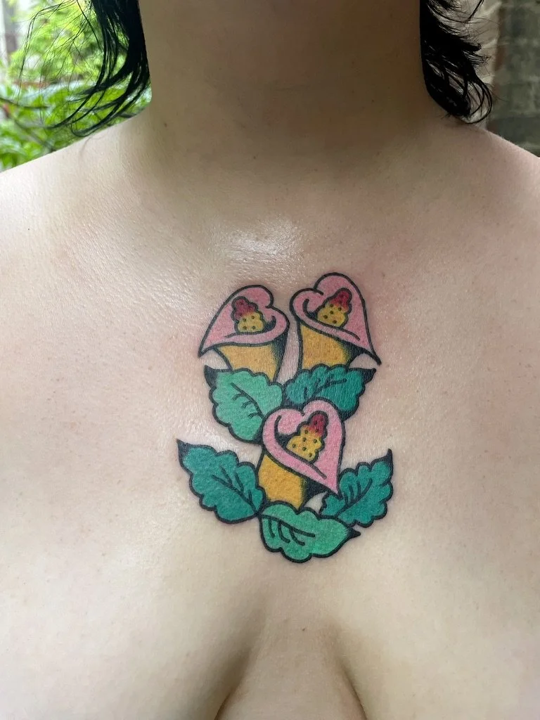 Tattoo of three pink hearts with yellow chicks inside, surrounded by green leaves on a person's chest.