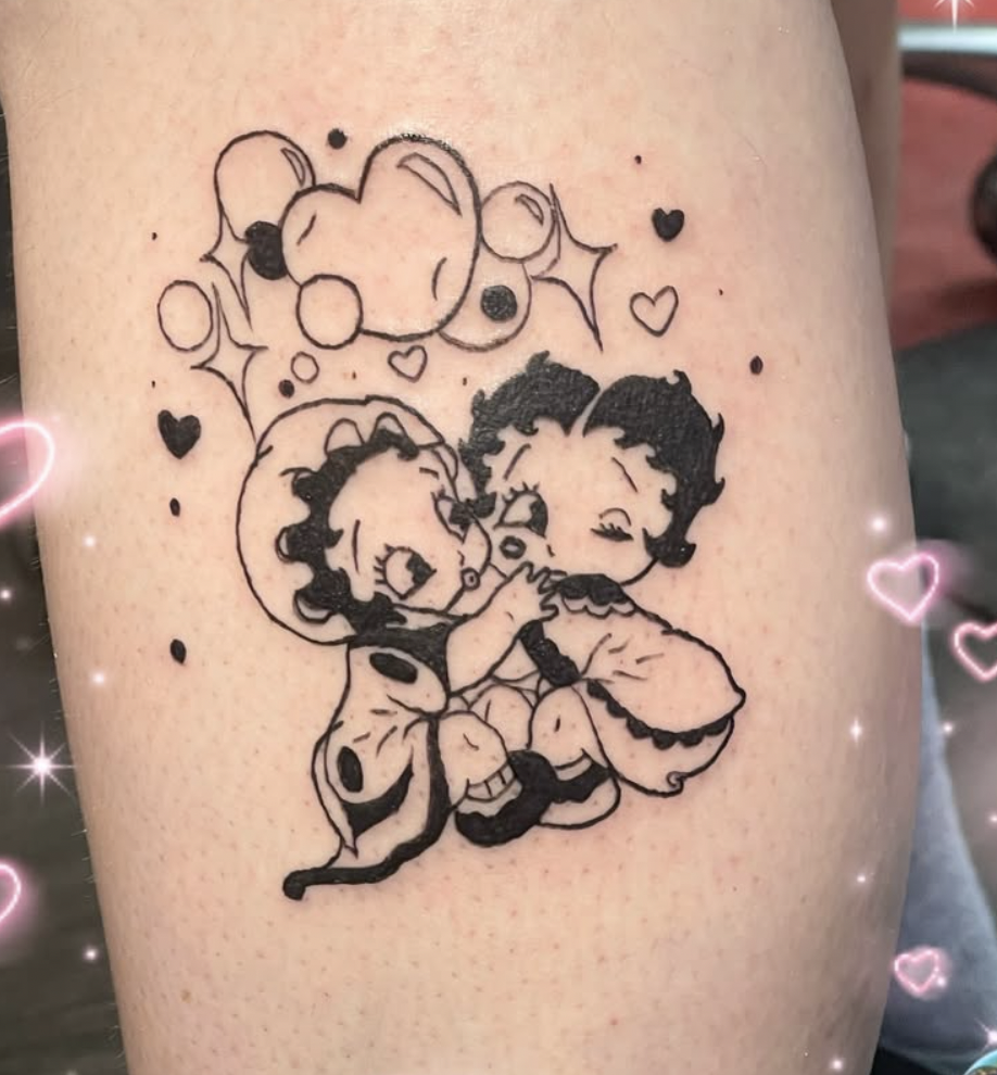 Tattoo of two cartoon children, a boy and girl, with flying butterfly and small hearts around them, in black ink.