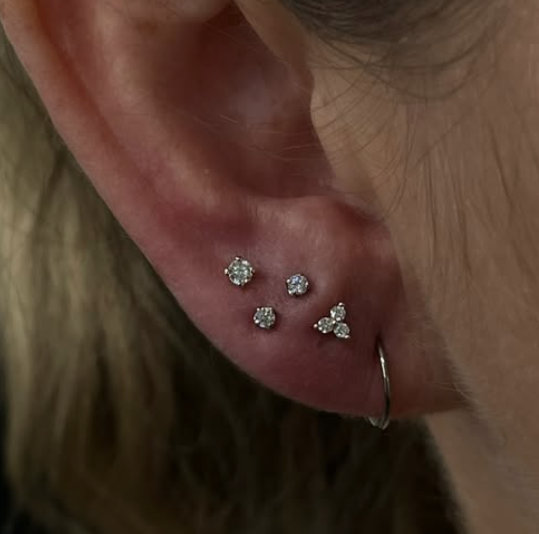 Close-up of a woman's ear with four small diamond stud earrings and a small hoop earring.