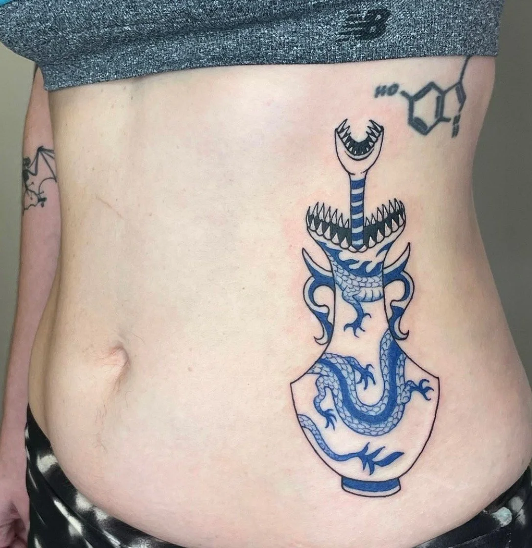 Tattoo of a blue dragon inside a vase on person's lower abdomen