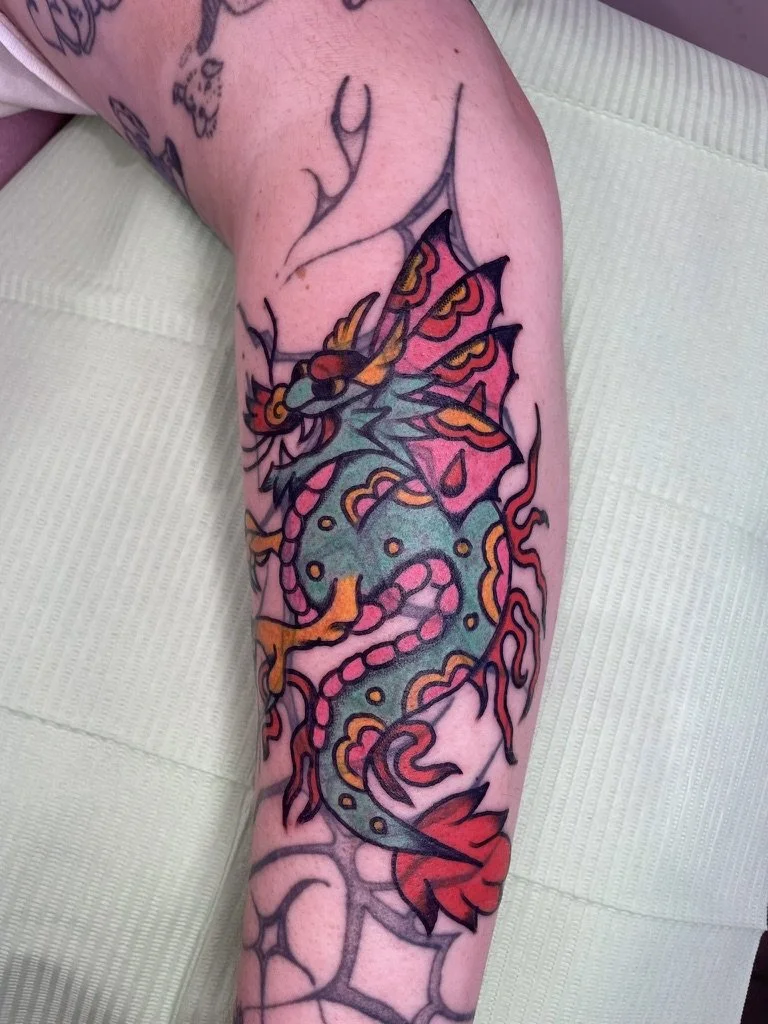 Colorful tattoo of a dragon with vibrant fins, surrounded by flames, on a person's leg.