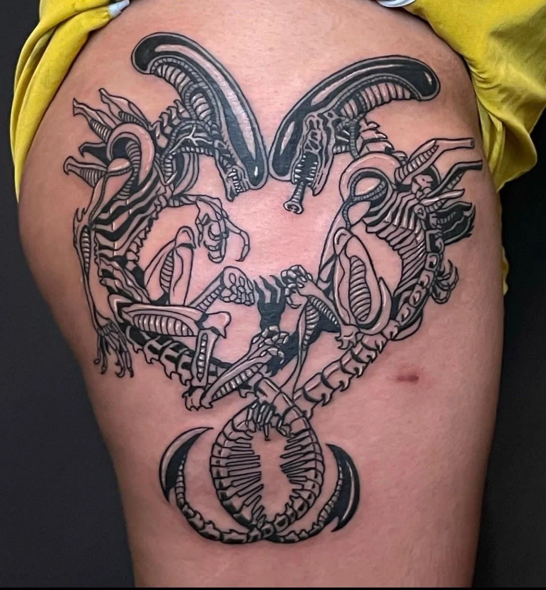 Tattoo of a heart shape made from intertwined scorpion and snake designs on a person's upper thigh.