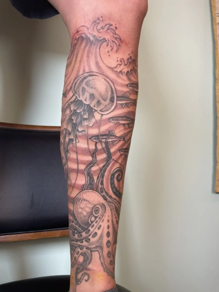 Tattoo of an ocean scene with a jellyfish, several small fish, and an octopus tentacle on a person's arm.