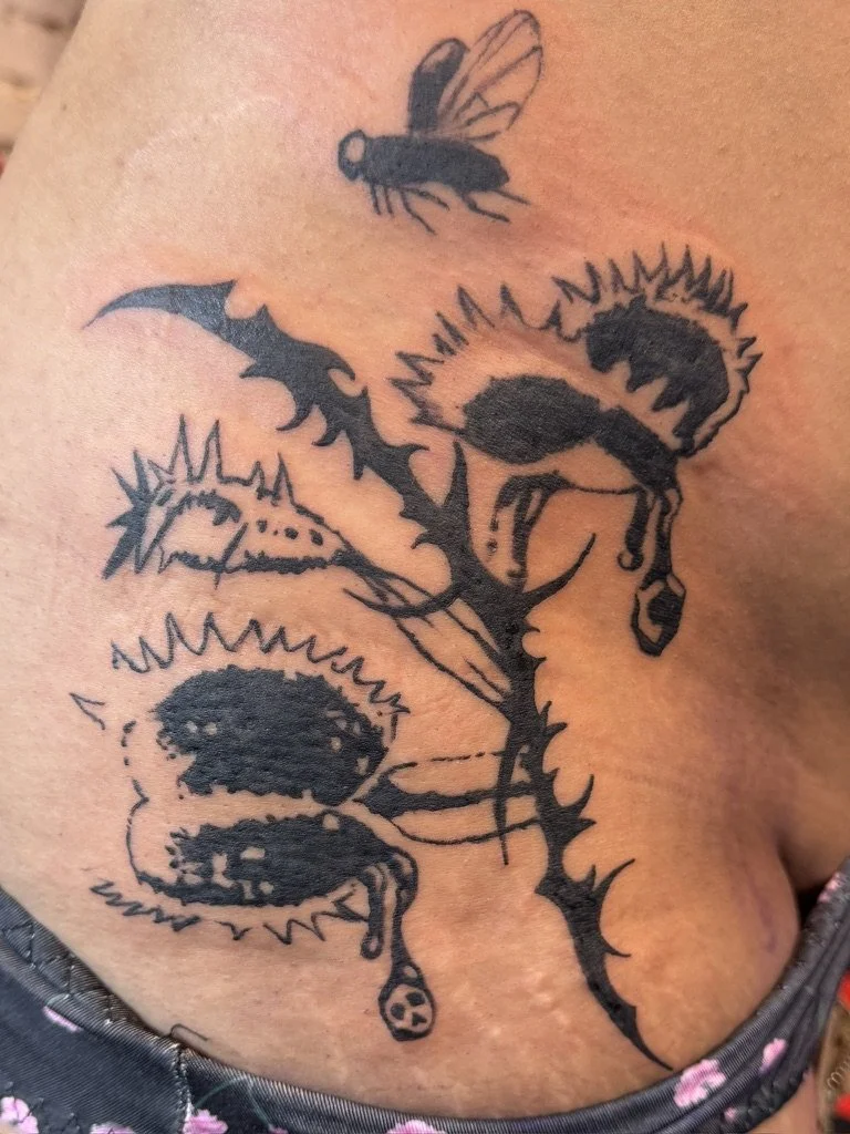 A black tattoo of a dragon with spiky features on a person's skin, accompanied by a bee flying above.