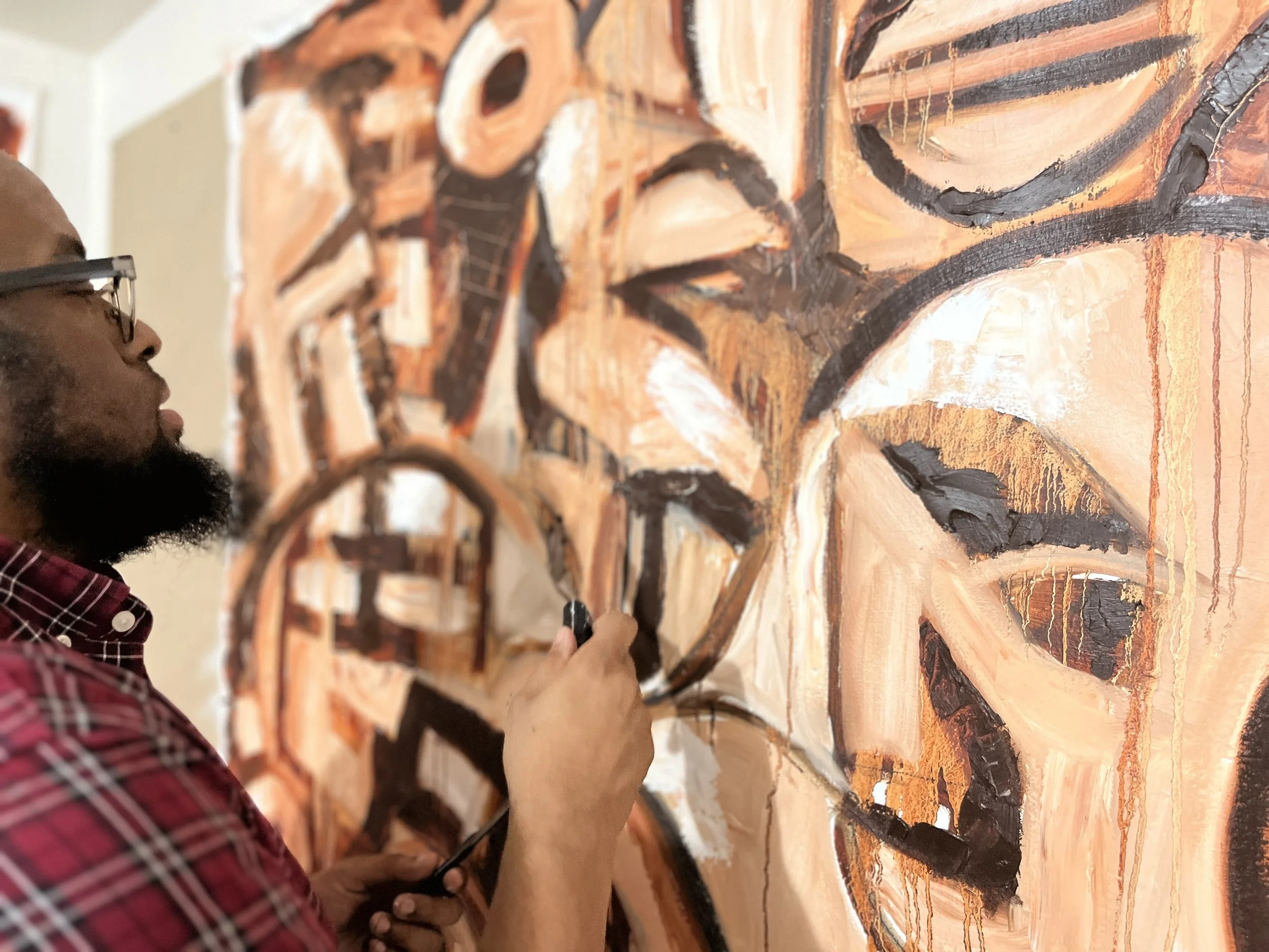 An artist painting a large mural with abstract face and word designs in shades of orange, black, and white.