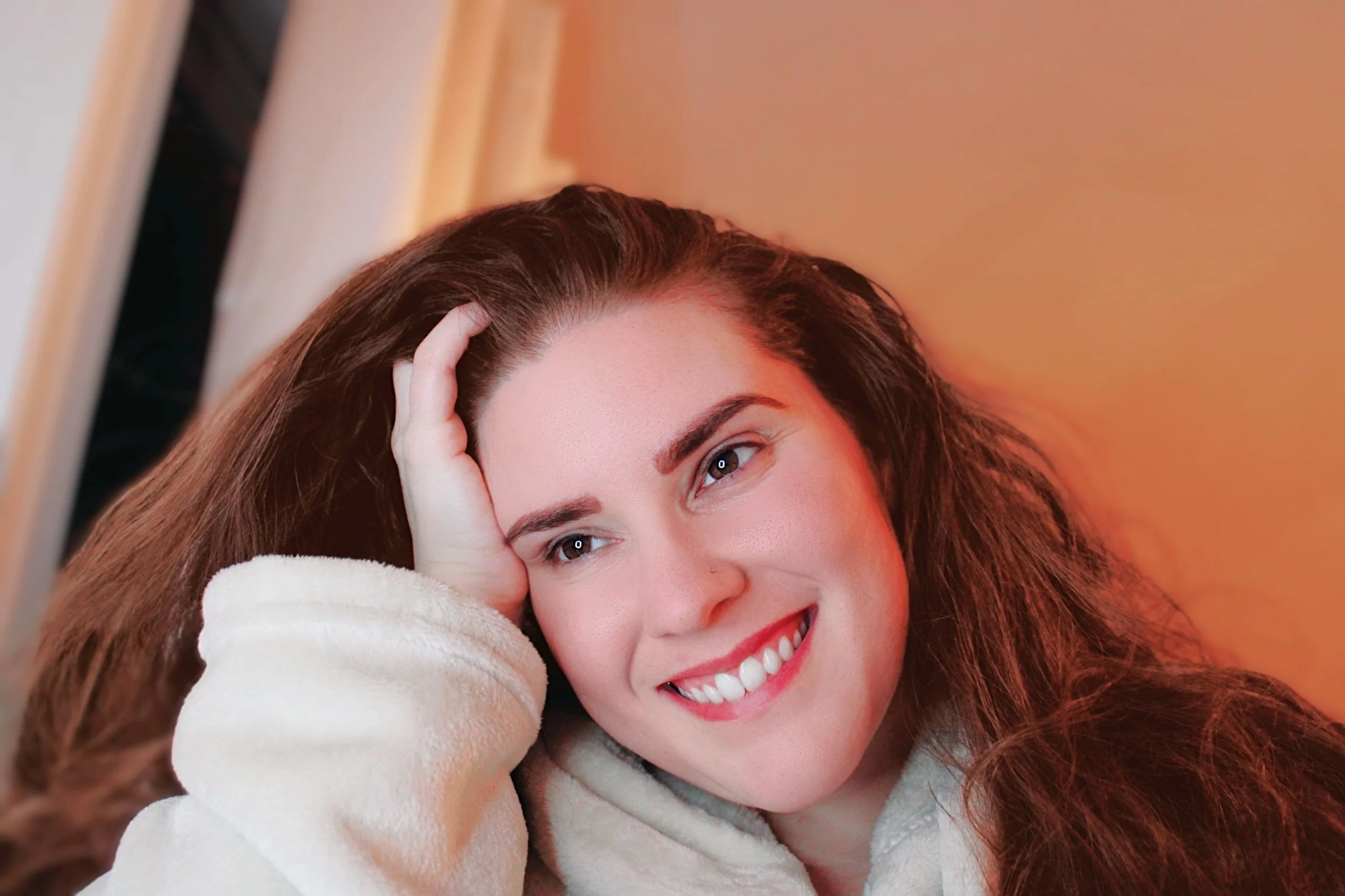 Close-up of a smiling person with long brown hair, resting their head on their hand.