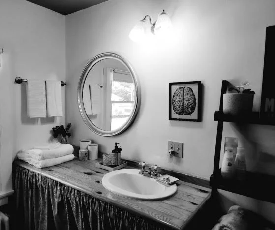 Bathroom with a wooden vanity, oval mirror, towel rack, and bookshelf