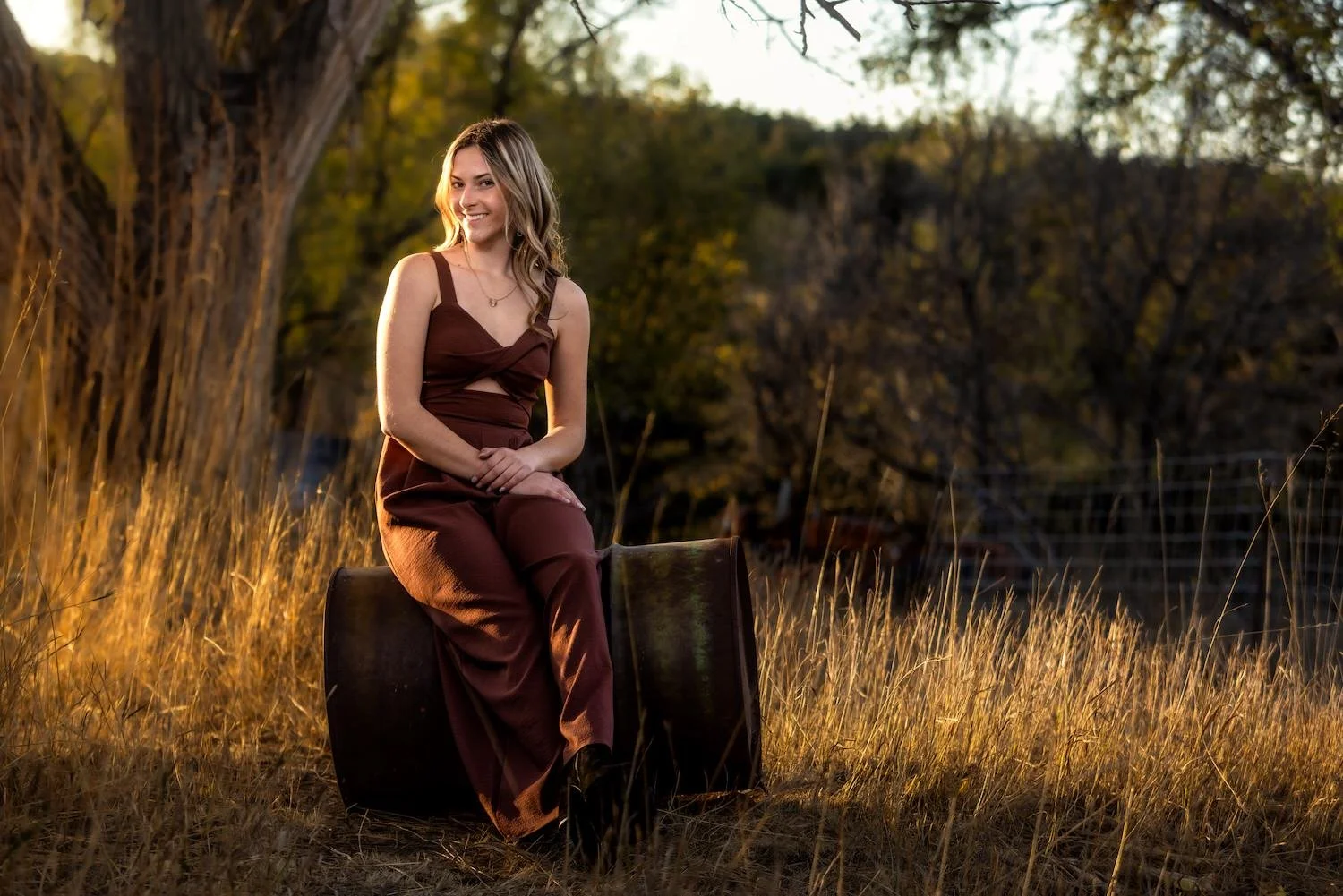 high school senior girl sitting on barrel at sunset in fall senior portrait