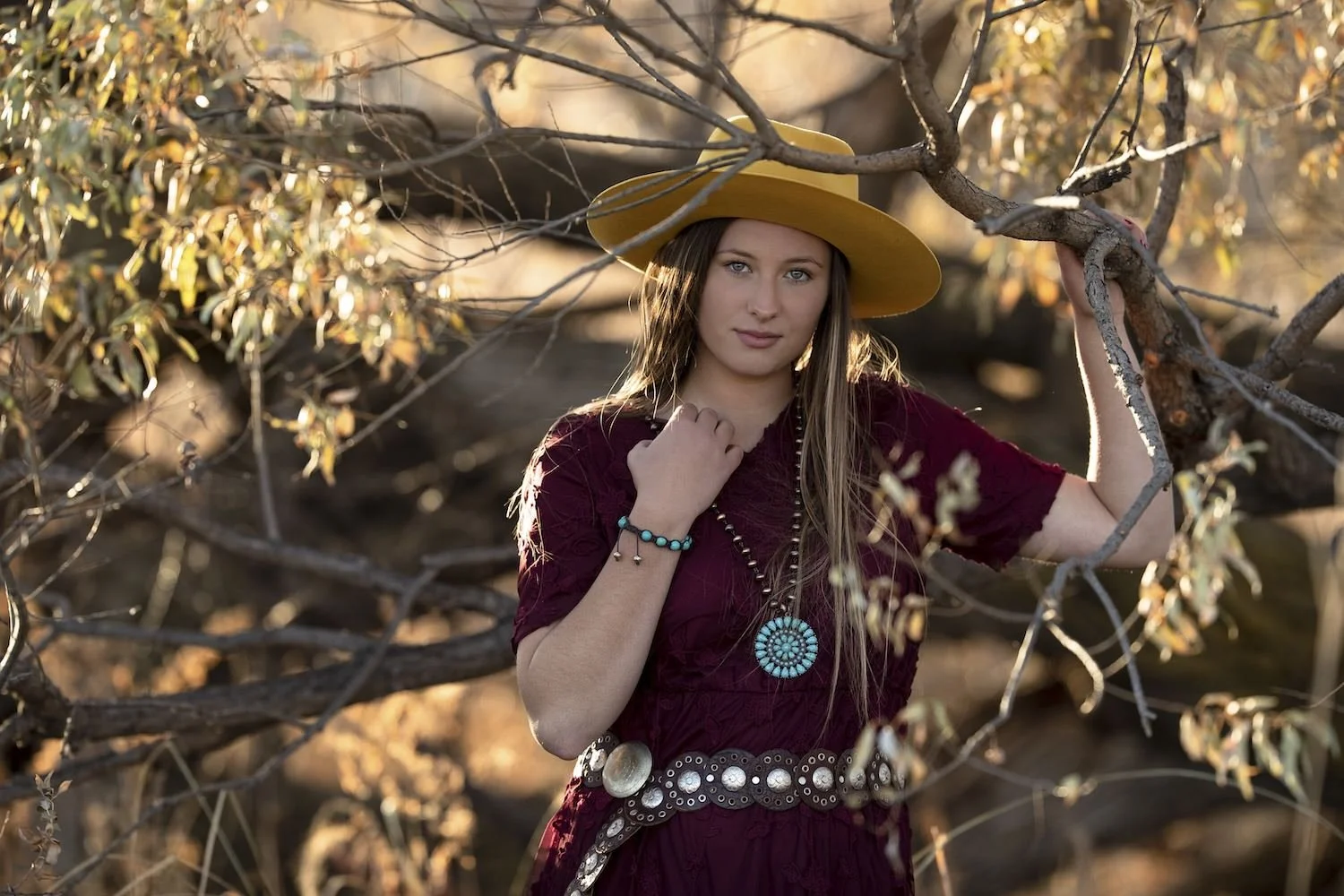high school senior girl in burgundy dress turquoise jewelry yellow felt hat at sunset