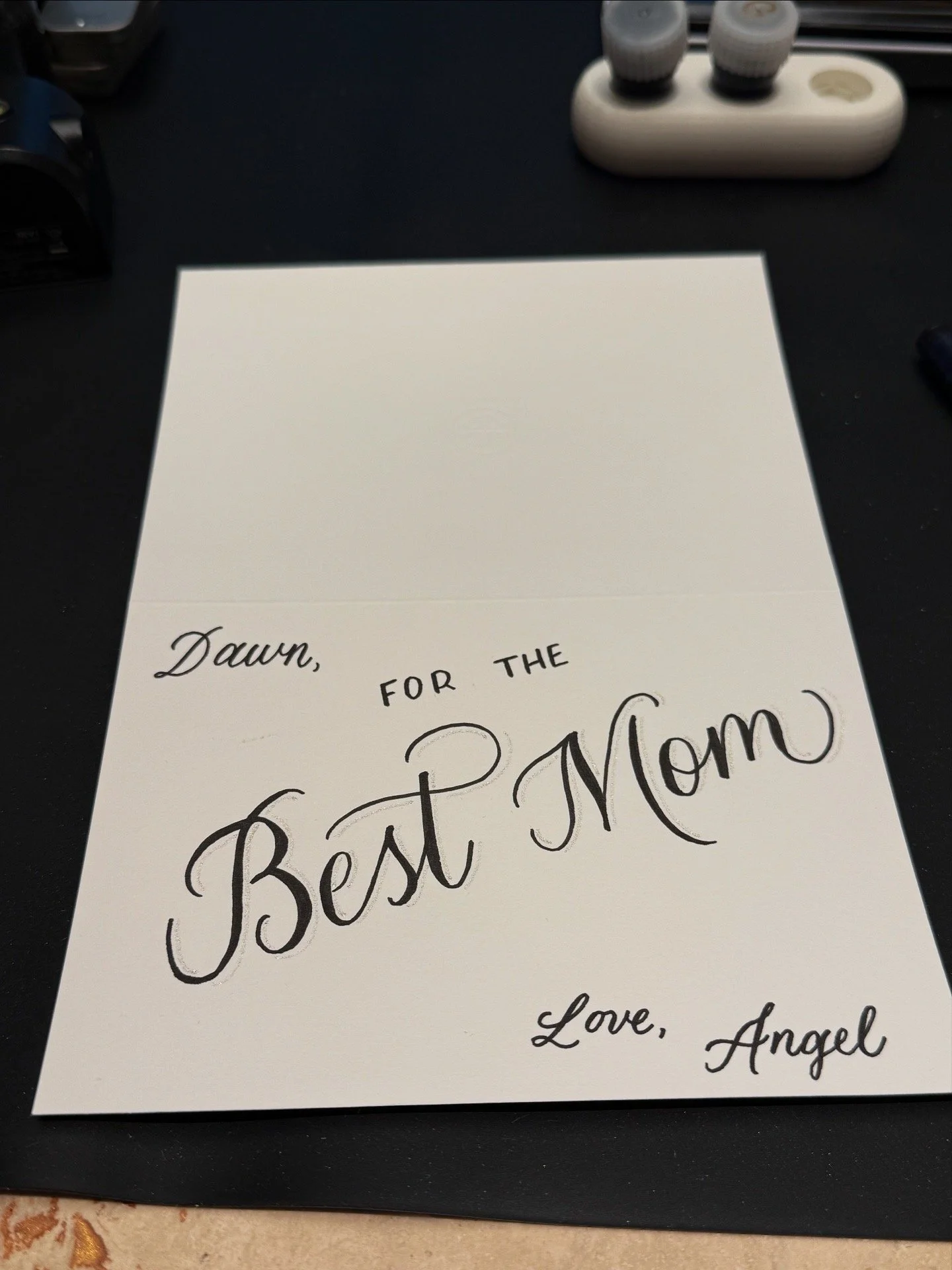 White notecard with black ink reading "Dawn, For the Best Mom Love, Angel" in a mix of script and print