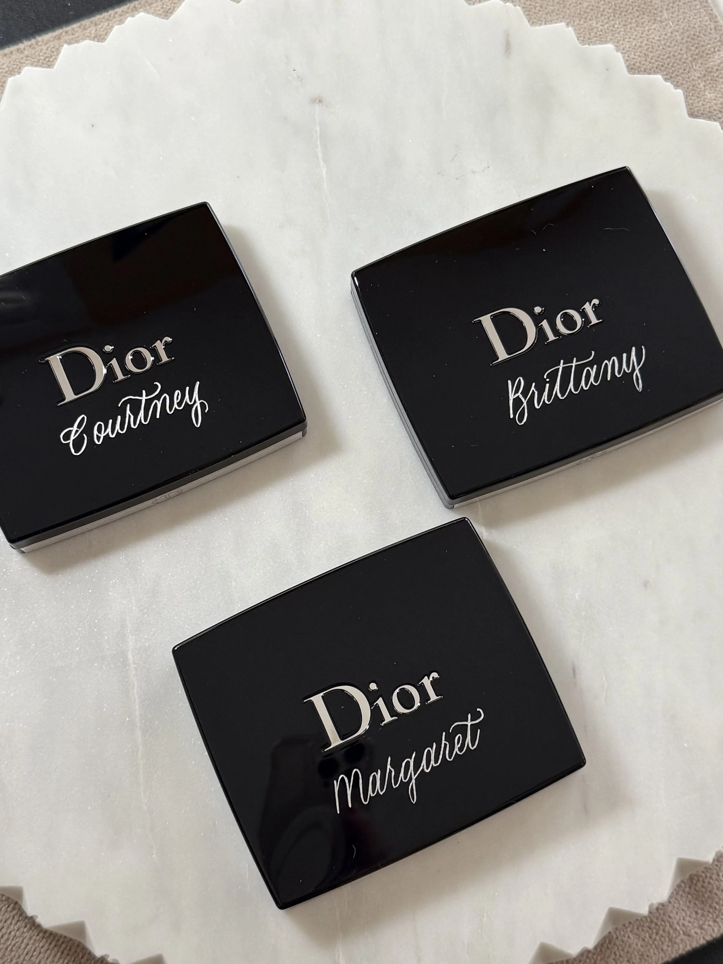 Three Dior compacts engraved with various names in silver calligraphy