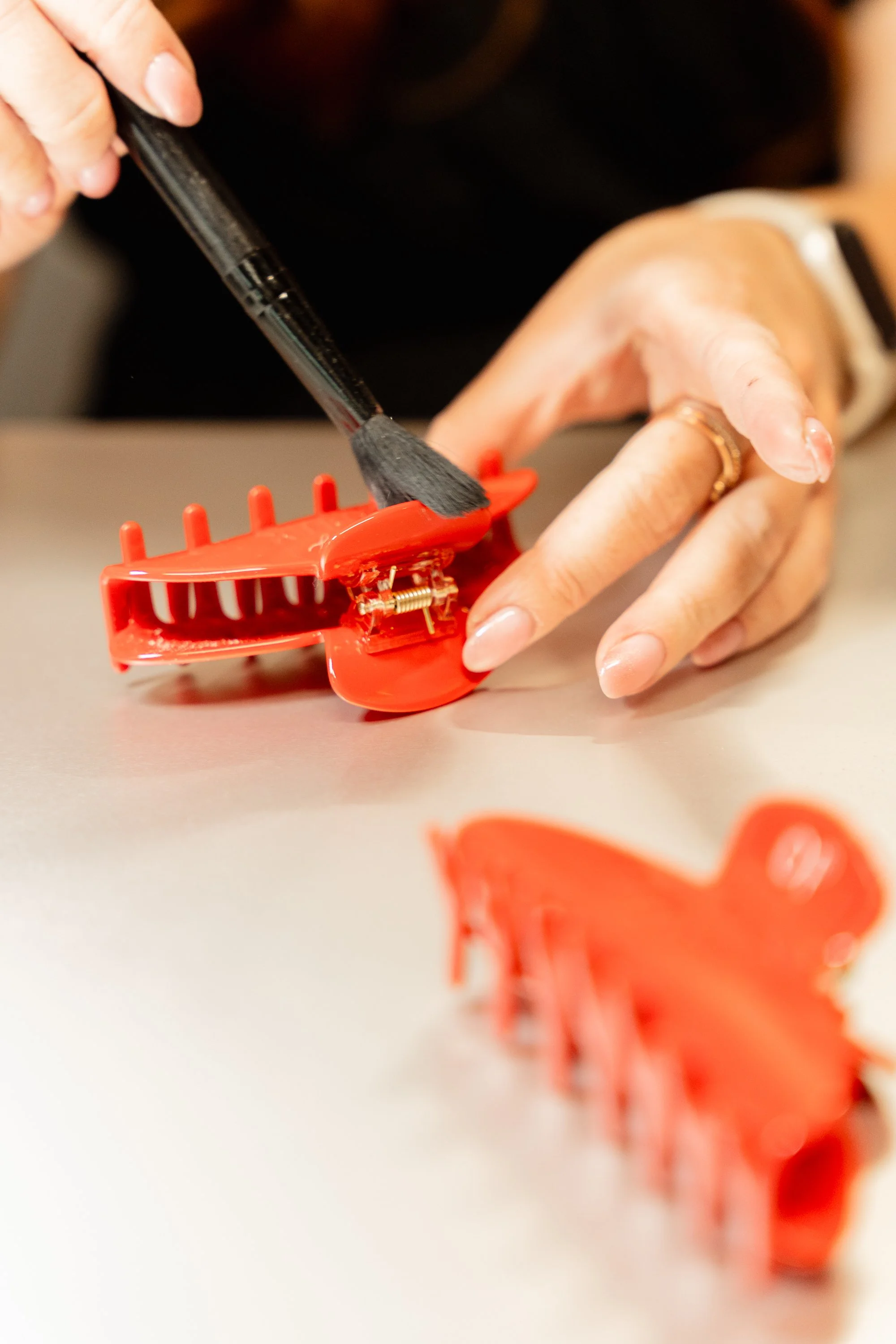 2 red Olaplex claw clips being personalized, one being brushed off with a black brush