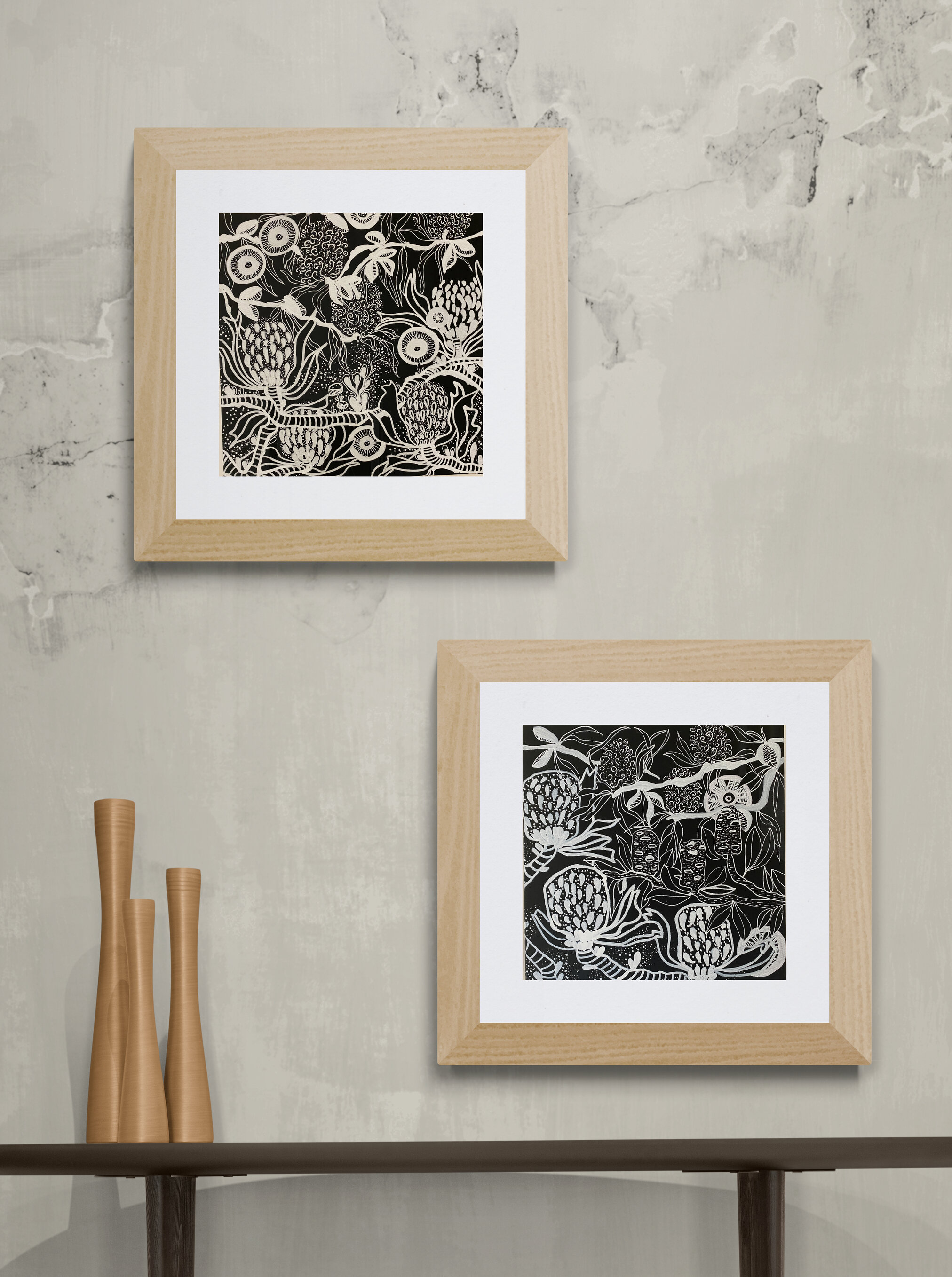 Two black and white botanical art prints framed in light wood on a textured light gray wall, with three tall tan vases on a dark wooden shelf below.