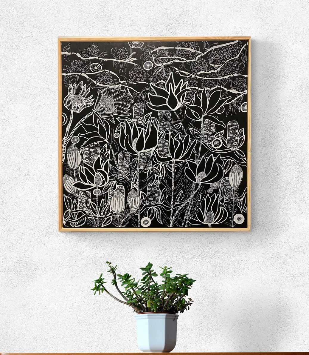 A modern interior with a framed black and white botanical line drawing hanging on a white textured wall above a white pot with green succulent plant on a wooden surface.