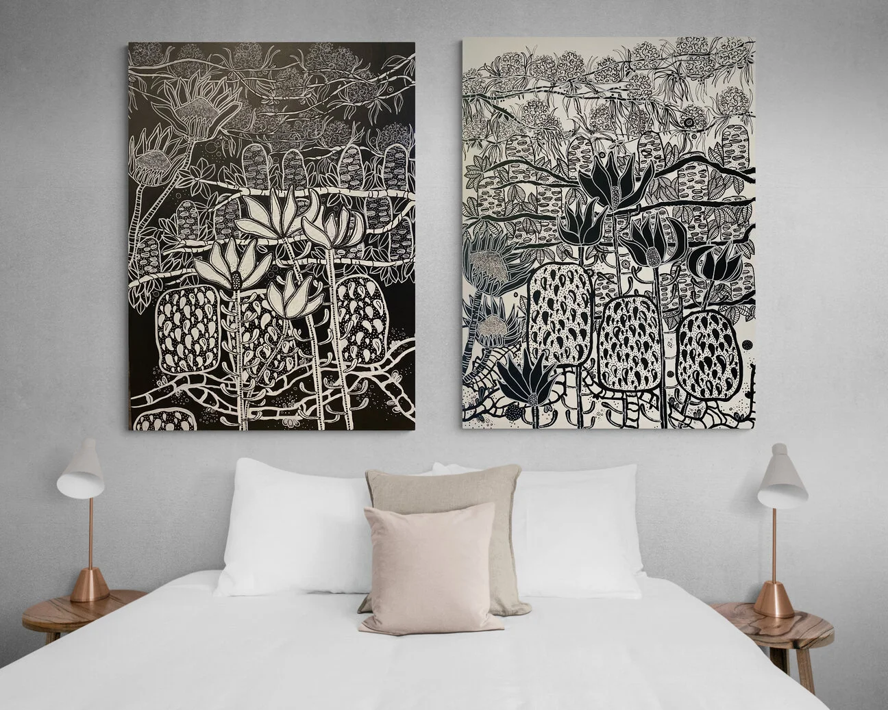 Two abstract black-and-white botanical art prints hanging above a bed with white and beige pillows, flanked by white table lamps on wooden nightstands.