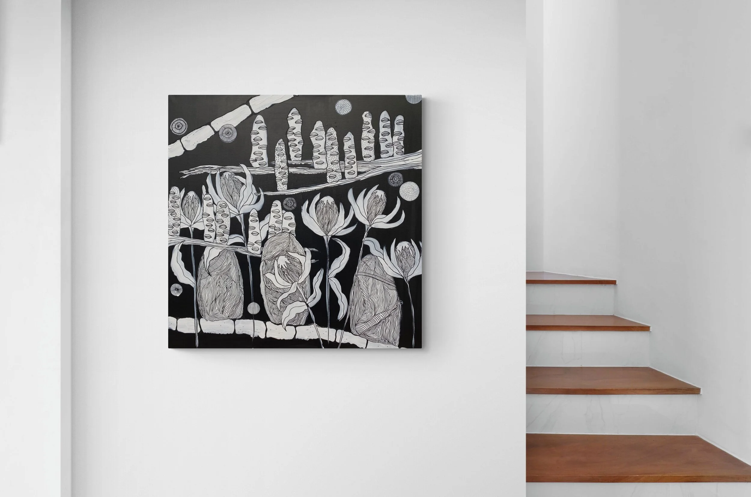 Black and white abstract painting on a wall, featuring organic shapes and lines. It's displayed next to a wooden staircase with white walls.