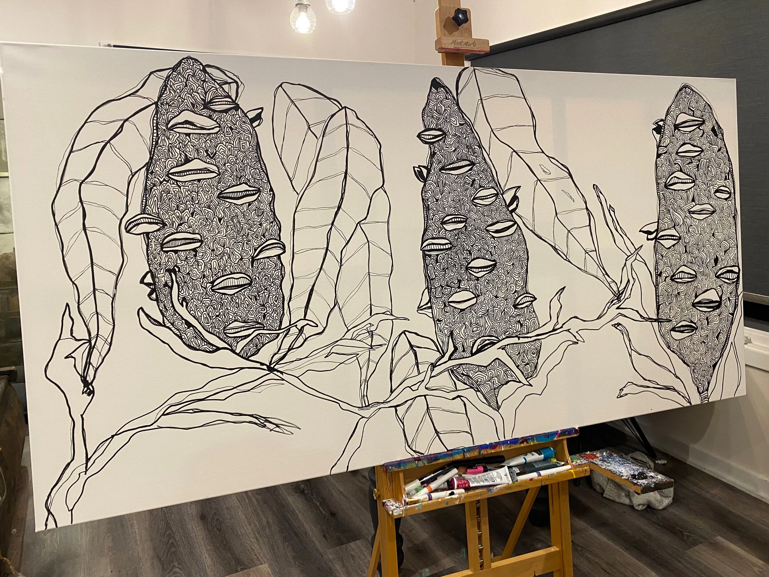 Illustrated artwork on a canvas depicting abstract plant shapes with leaves and eyes, outlined in black, on an easel.