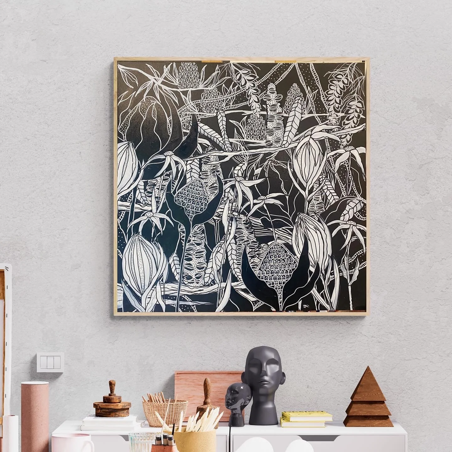 Wall art with black and white abstract floral design above a desk with various items including busts and a triangular sculpture.