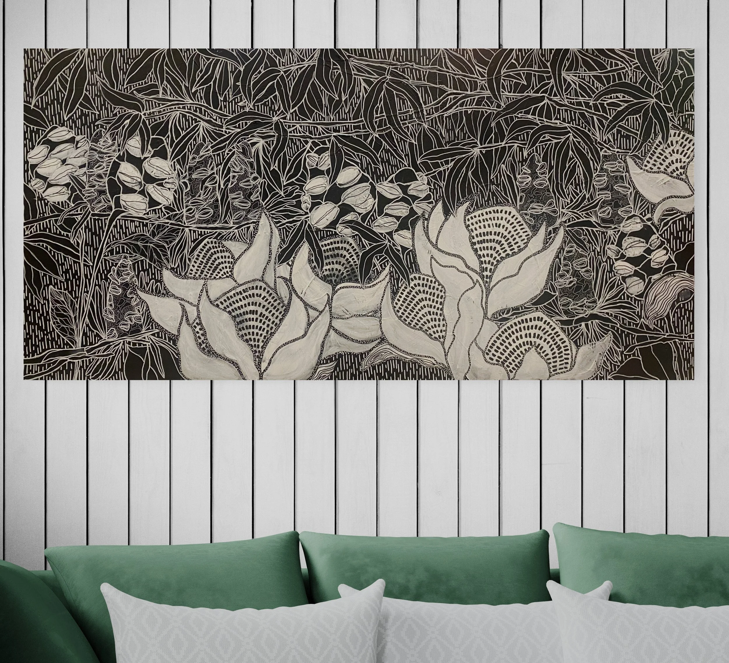 A black-and-white abstract floral artwork hangs above a bed with light green pillows and white pillows with a subtle pattern, set against white paneled walls.