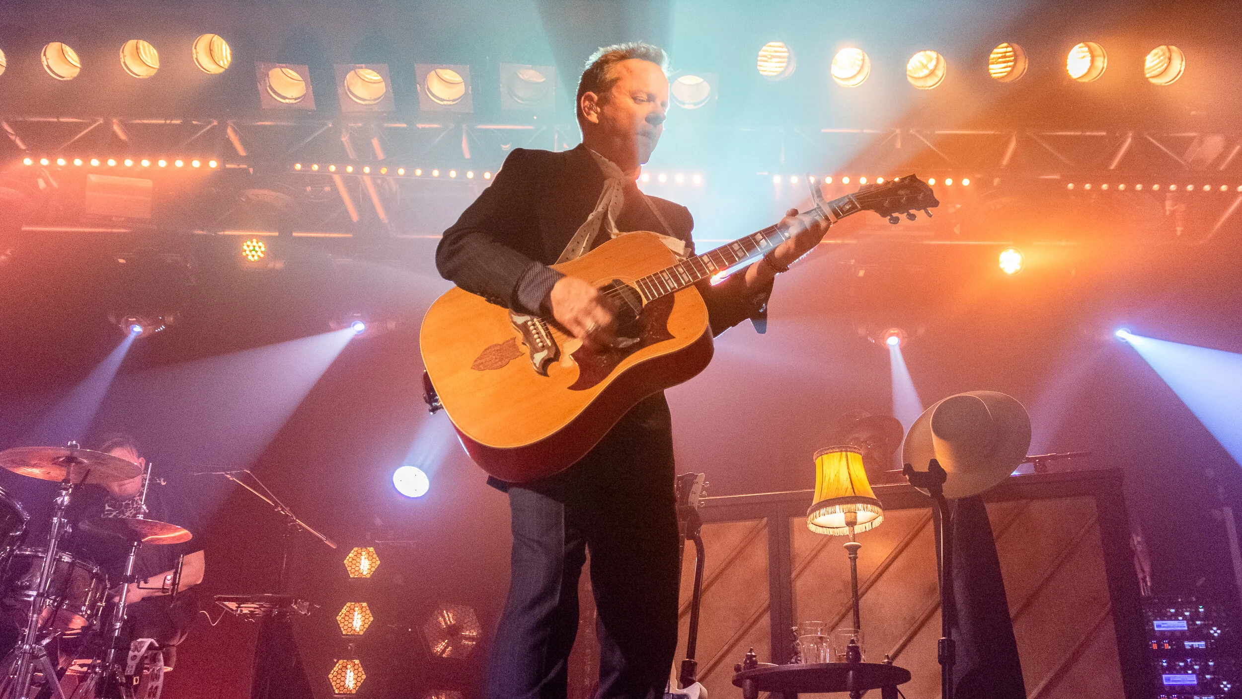Kiefer Sutherland playing acoustic guitar under a bank of stage lights at the O2 Academy Oxford