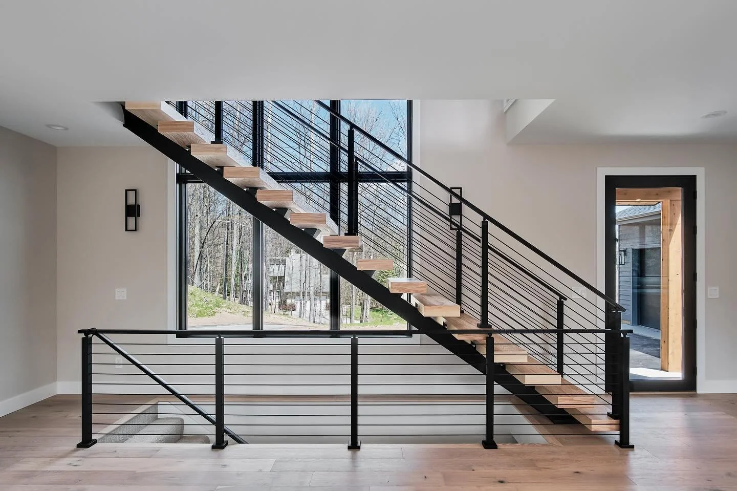 Using a floating steel staircase allows us to make an open connection between floors, while also showcasing these stunning two story windows. #builder#homebuilder#architecture#traversecity#leelanau