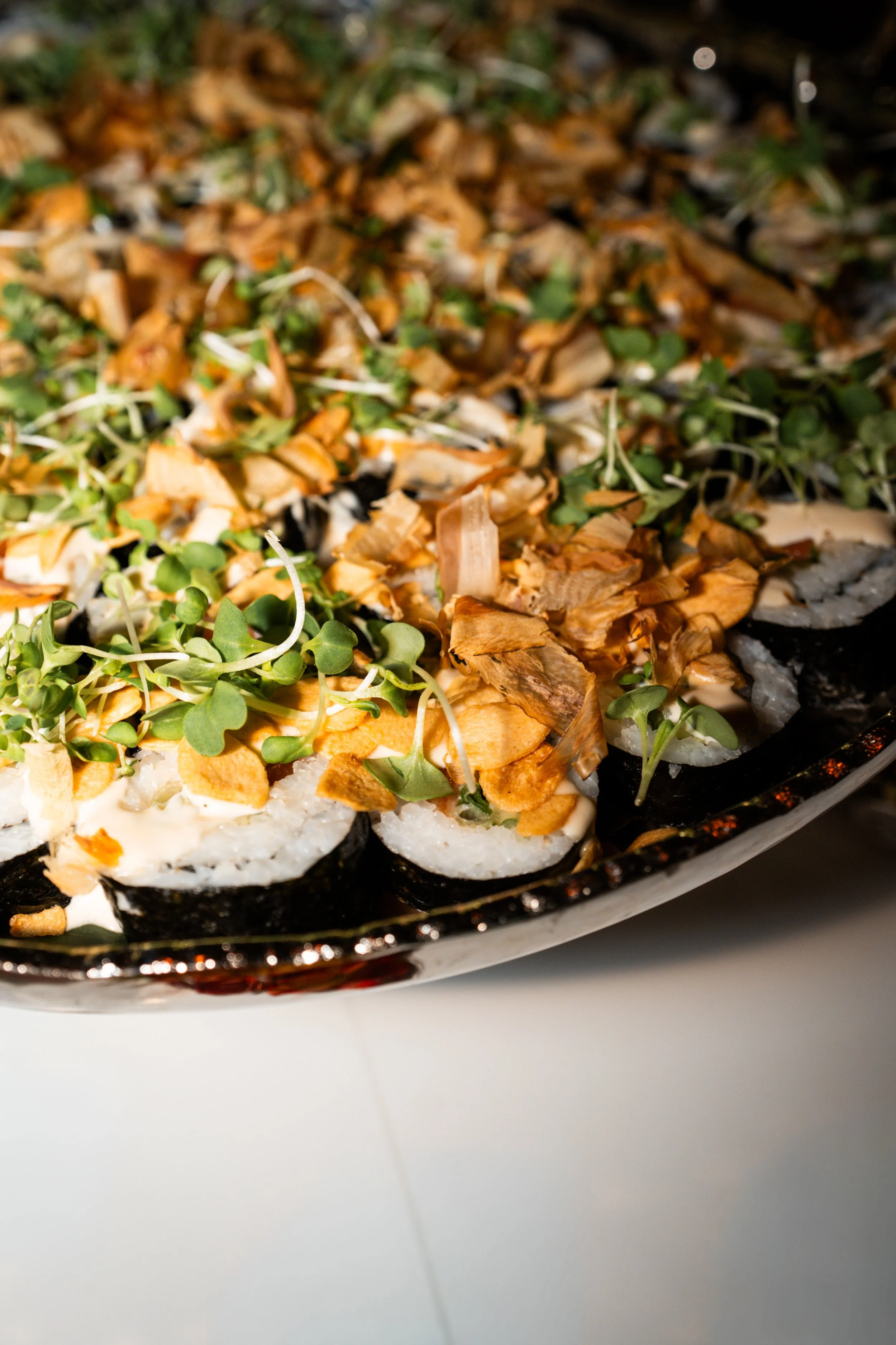Close-up of a platter of sushi topped with microgreens and fried garlic slices.
