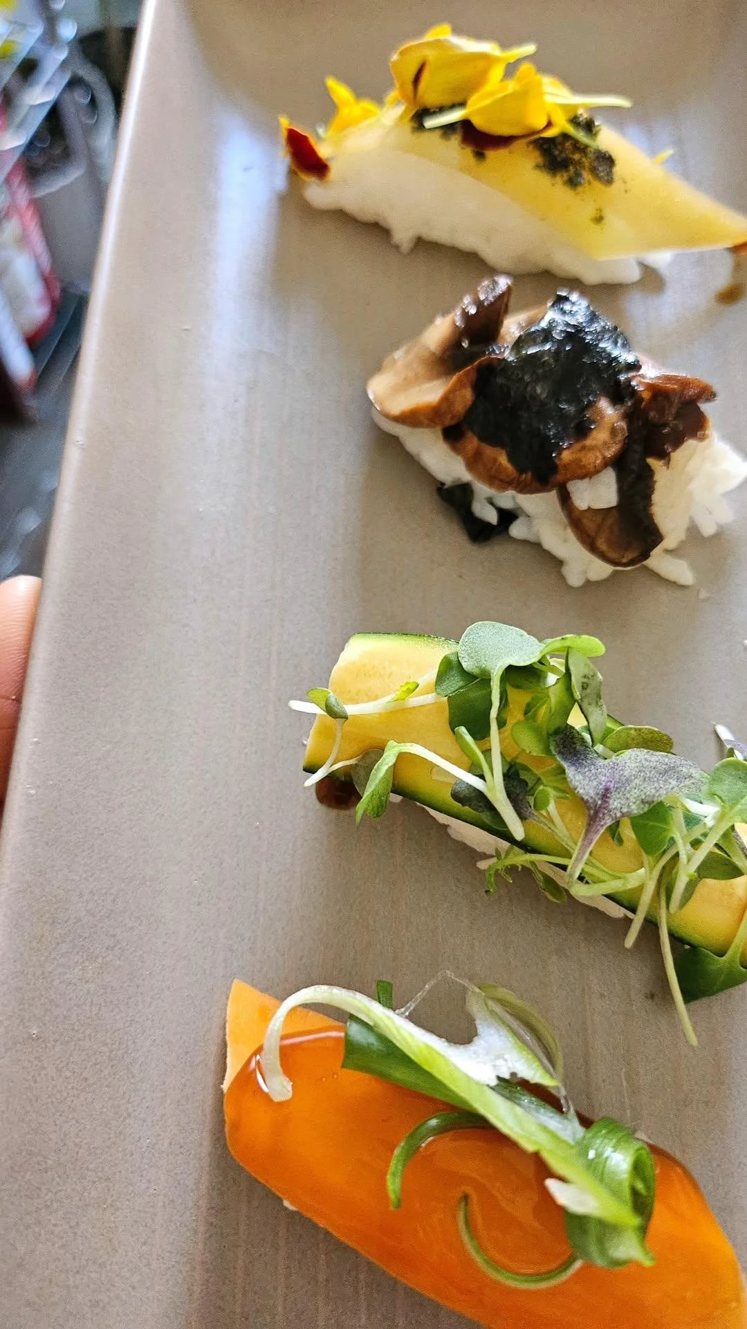 Four pieces of sushi with various toppings and garnishes arranged on a beige surface.