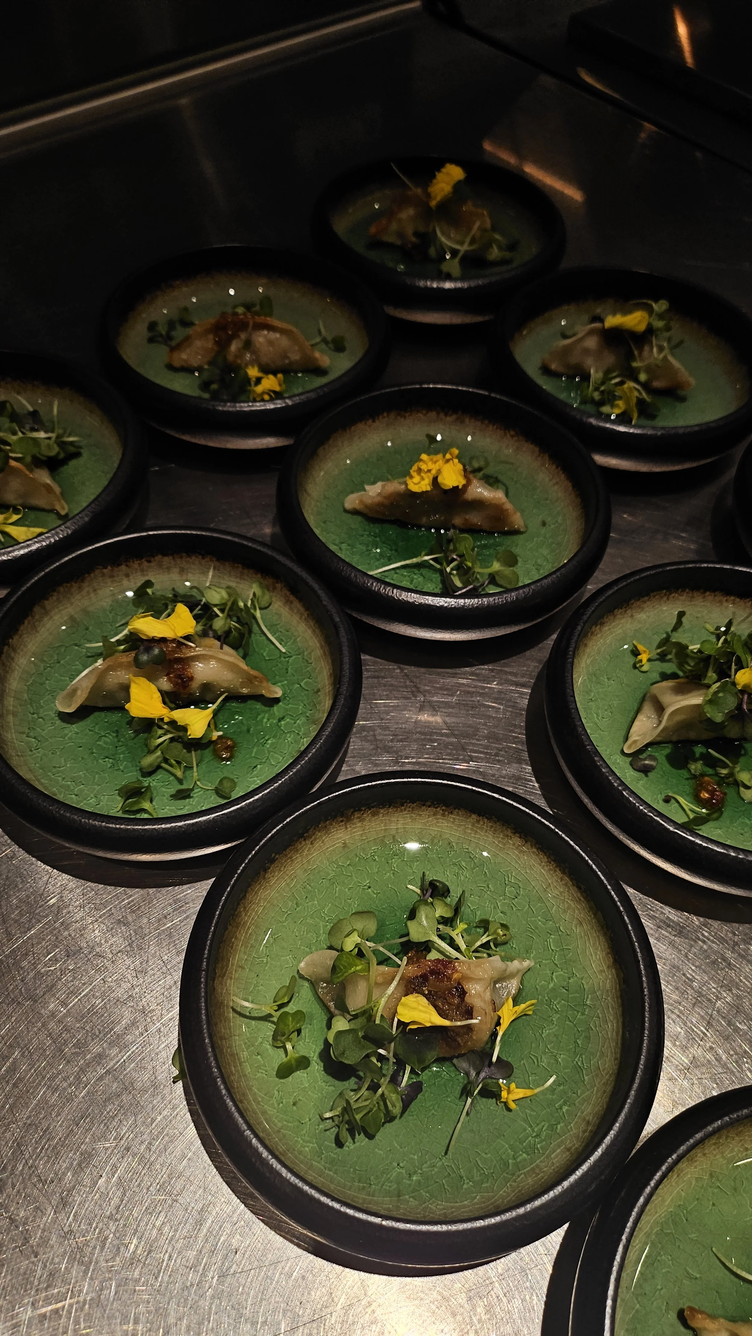 Elegant plates with a green sauce, topped with a piece of meat or fish, microgreens, and yellow edible flowers.