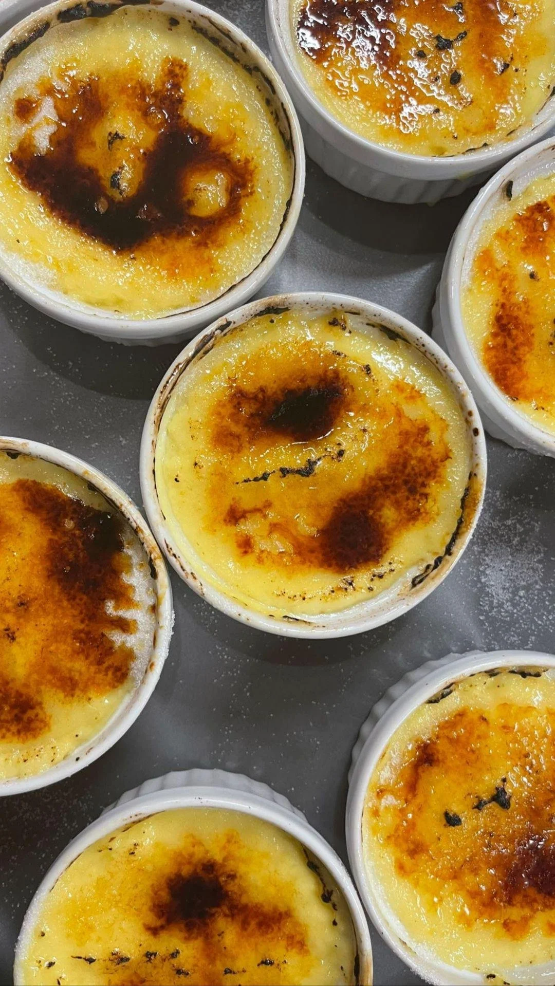 Close-up of several baked custards with caramelized sugar on top, in ramekins.