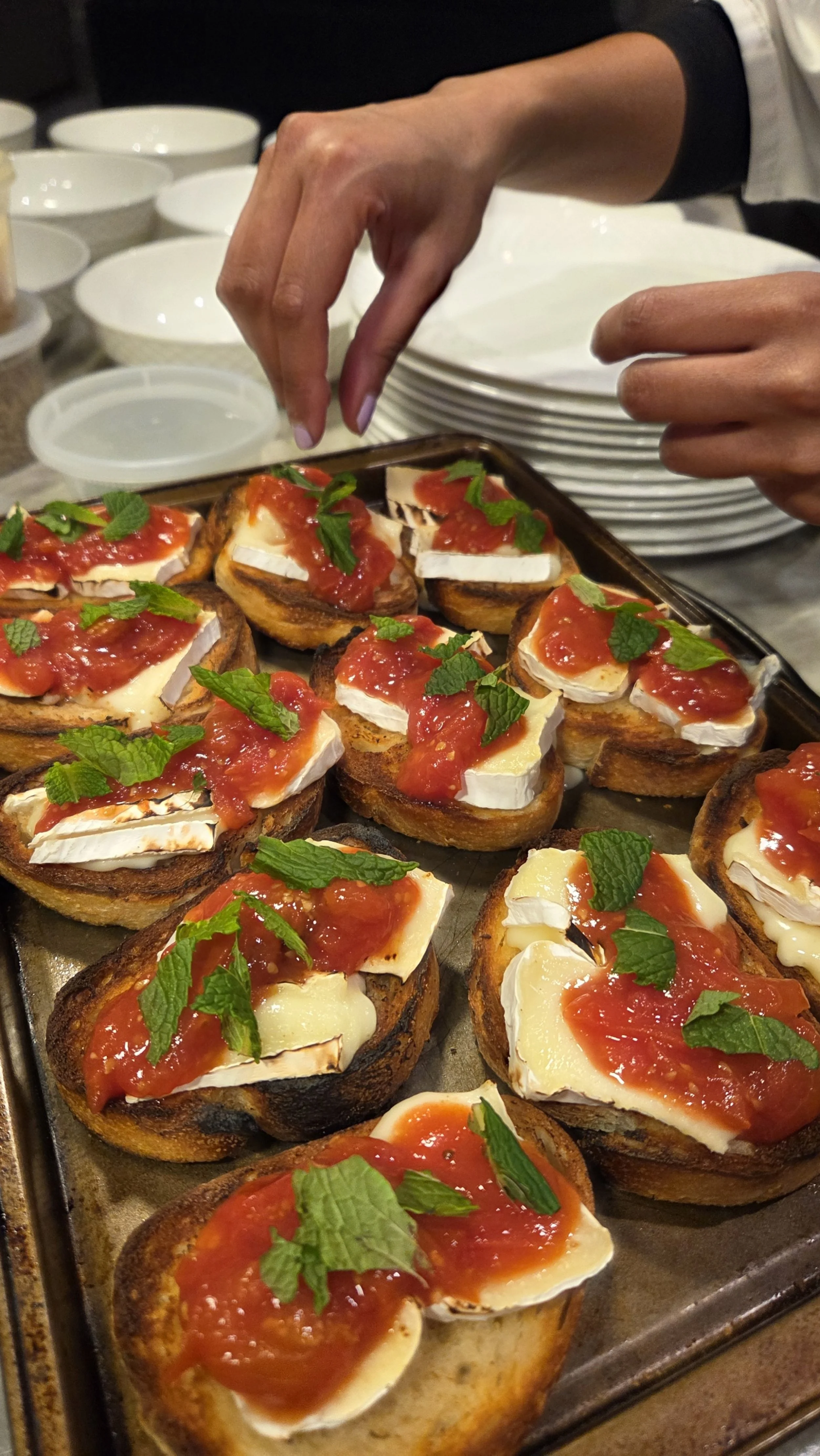 Person garnishing toasted bread with melted cheese, tomato sauce, and fresh mint leaves.