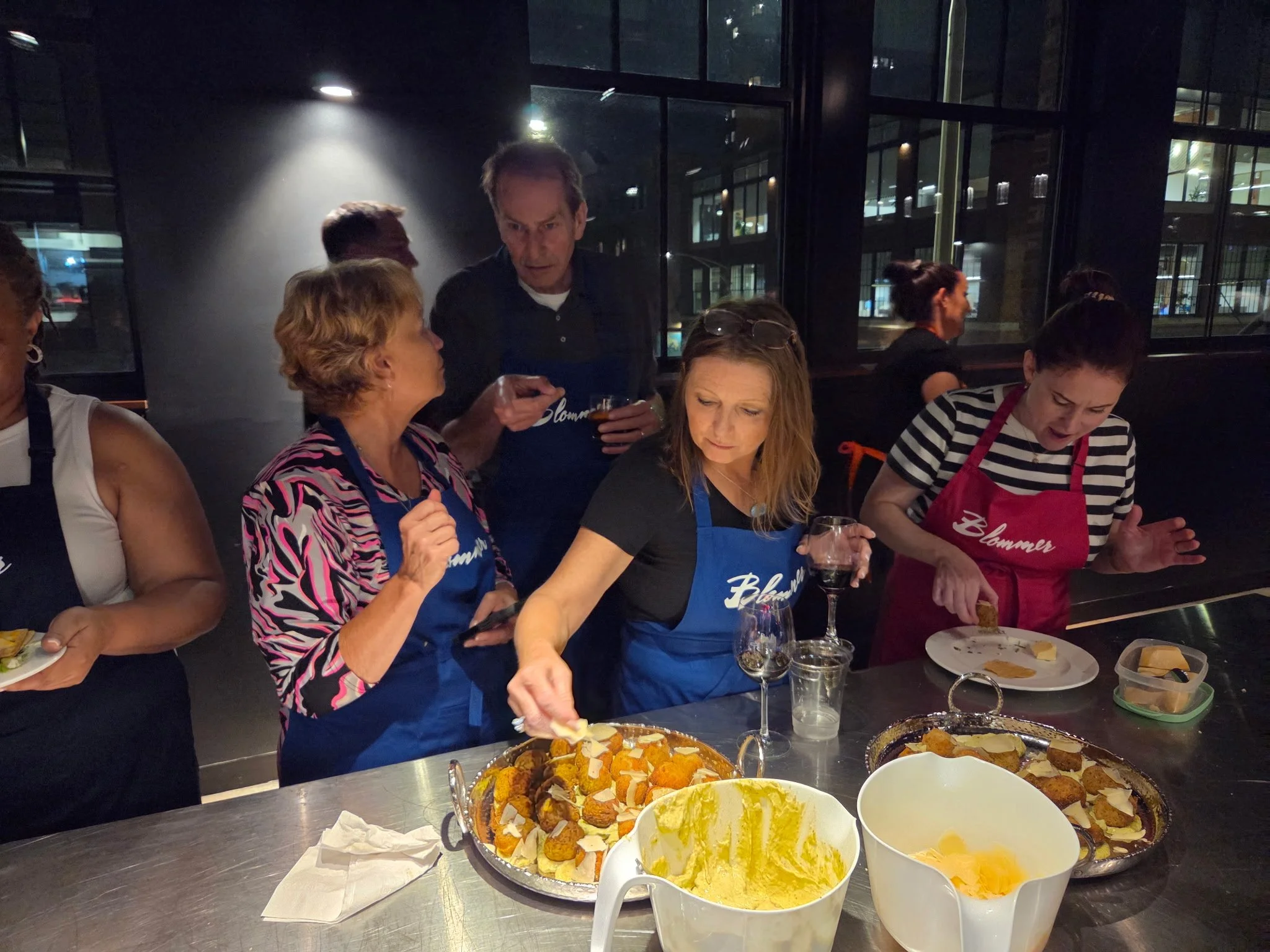 Group of people cooking and preparing food together in a kitchen at night.