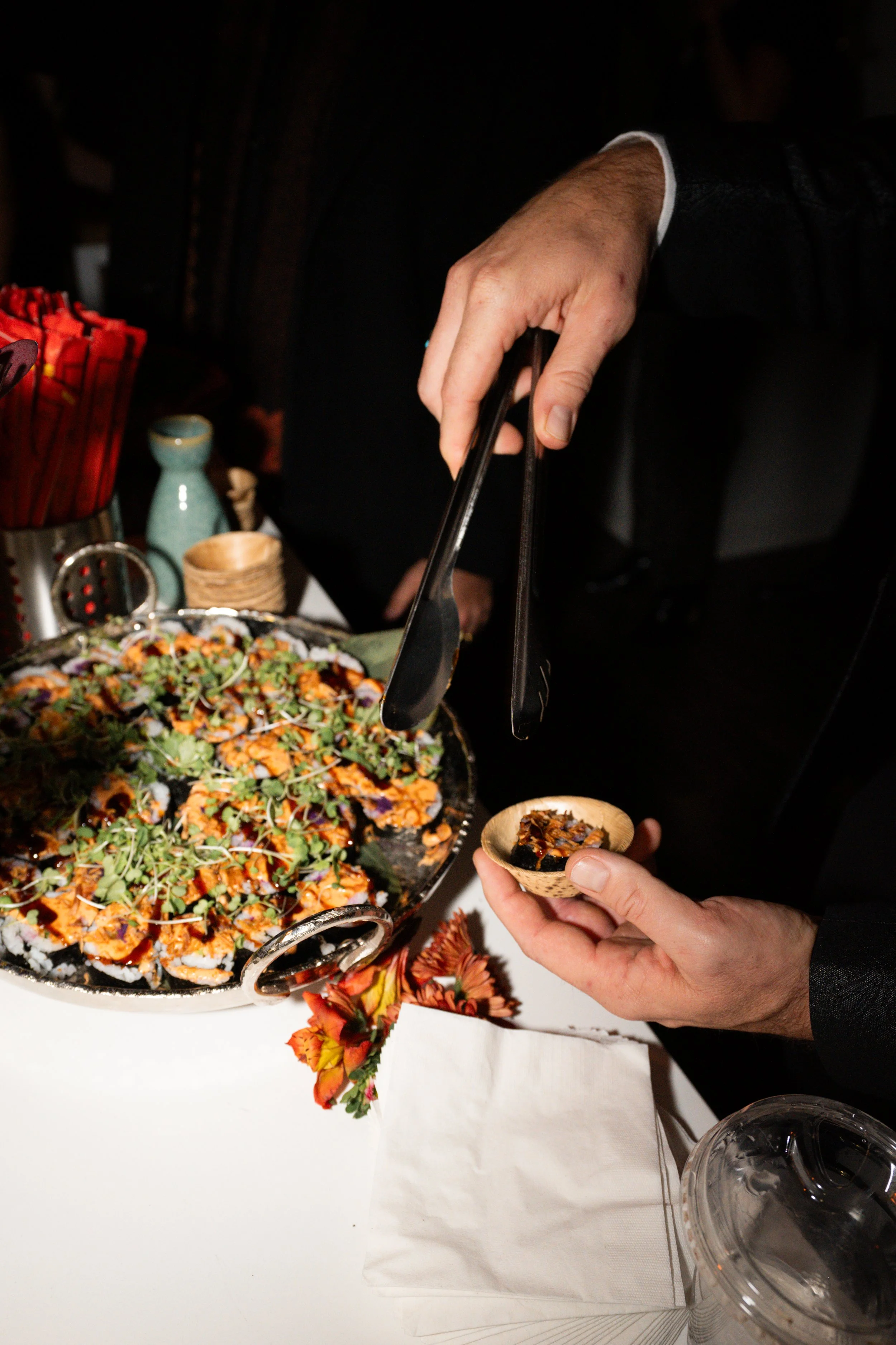 Person serving sushi from a large platter onto a small wooden bowl.