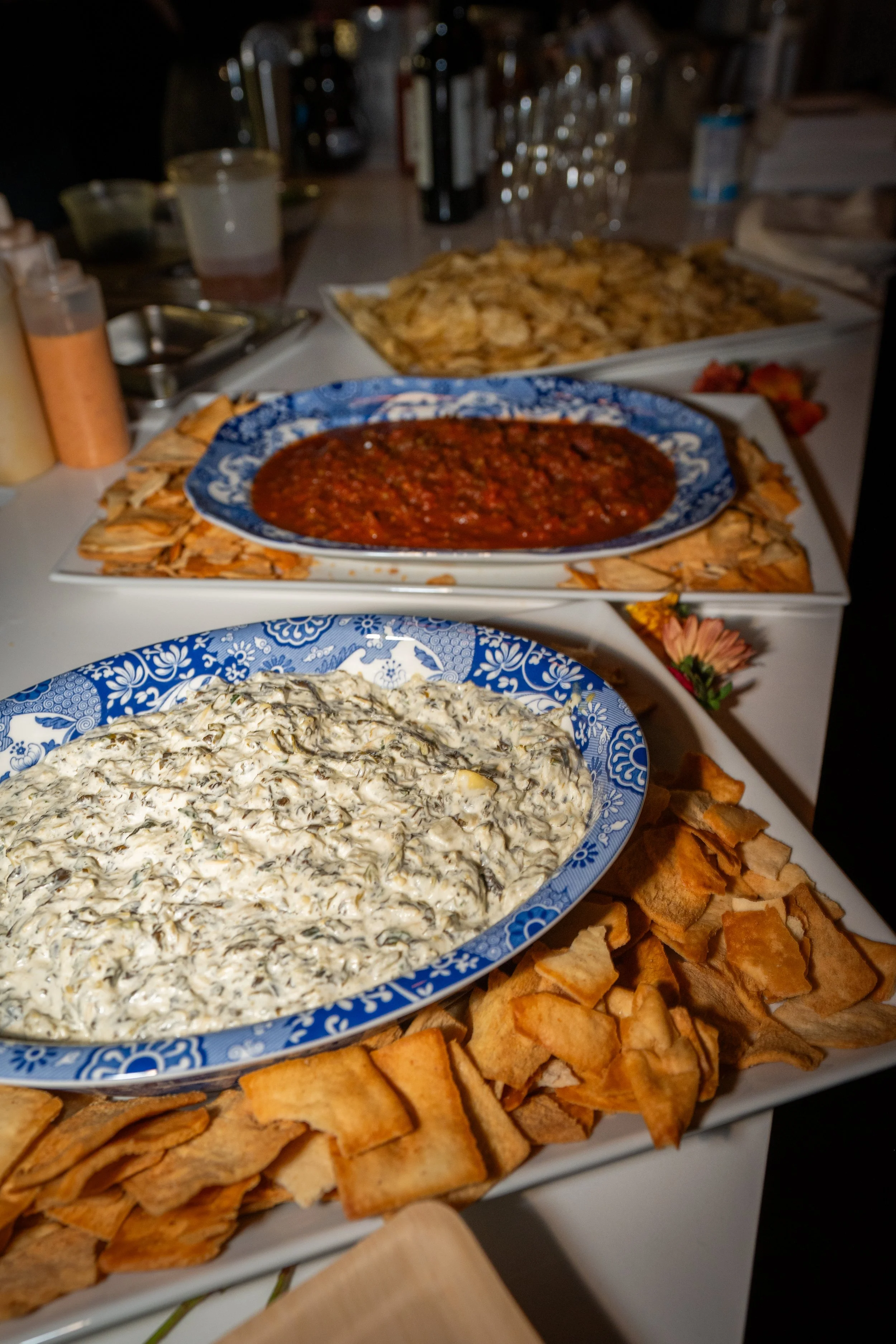 A table with various dishes including a bowl of spinach dip, a bowl of red chili, and a bowl of chicken salad, surrounded by chunks of toasted bread.