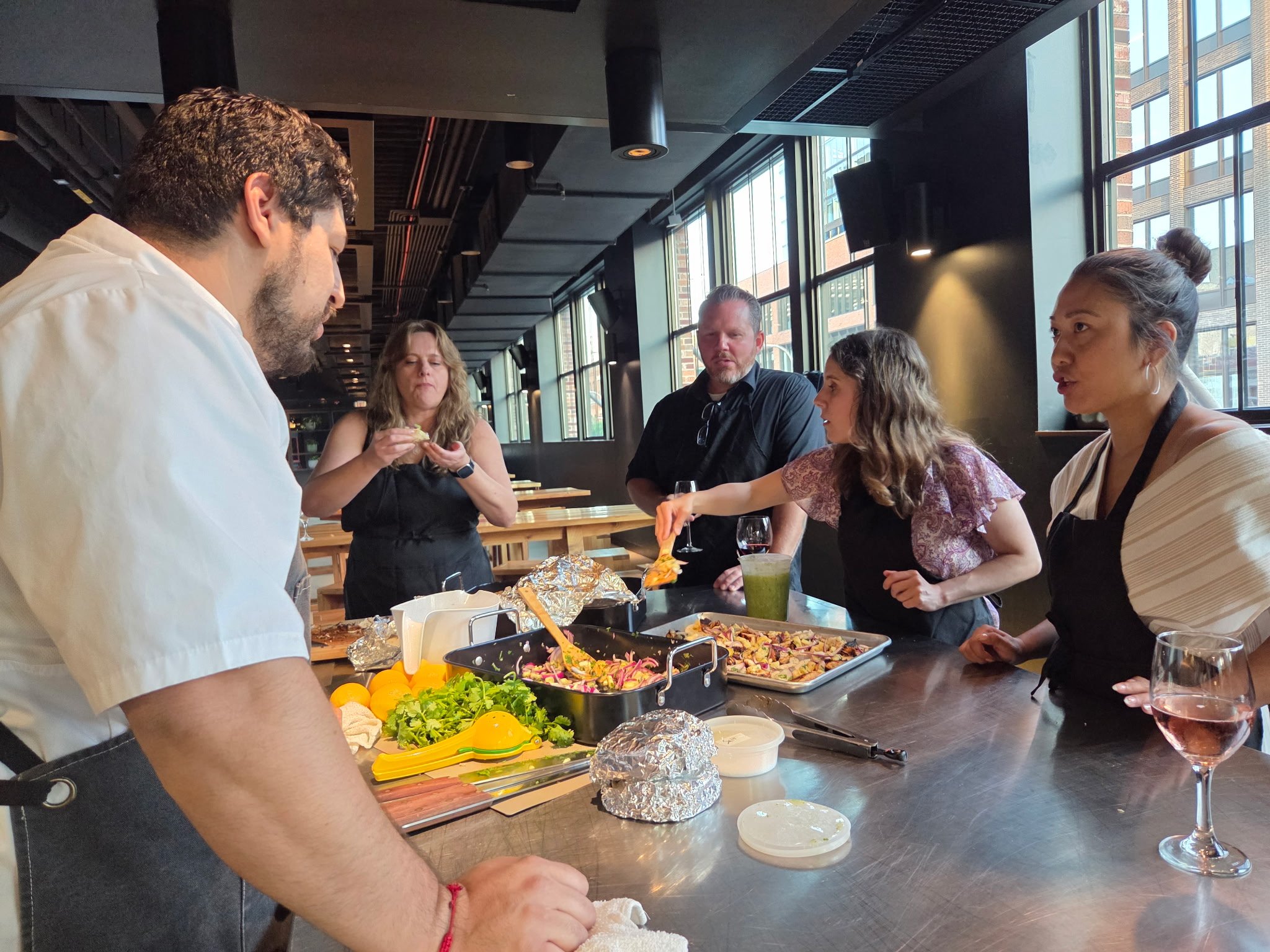 Group of five people in a restaurant preparing food, with ingredients and dishes on the table.