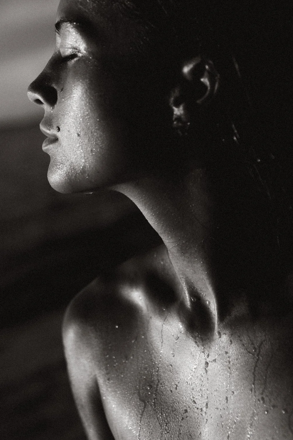Close-up side profile of a sweating woman with water droplets on her skin, black and white photo.