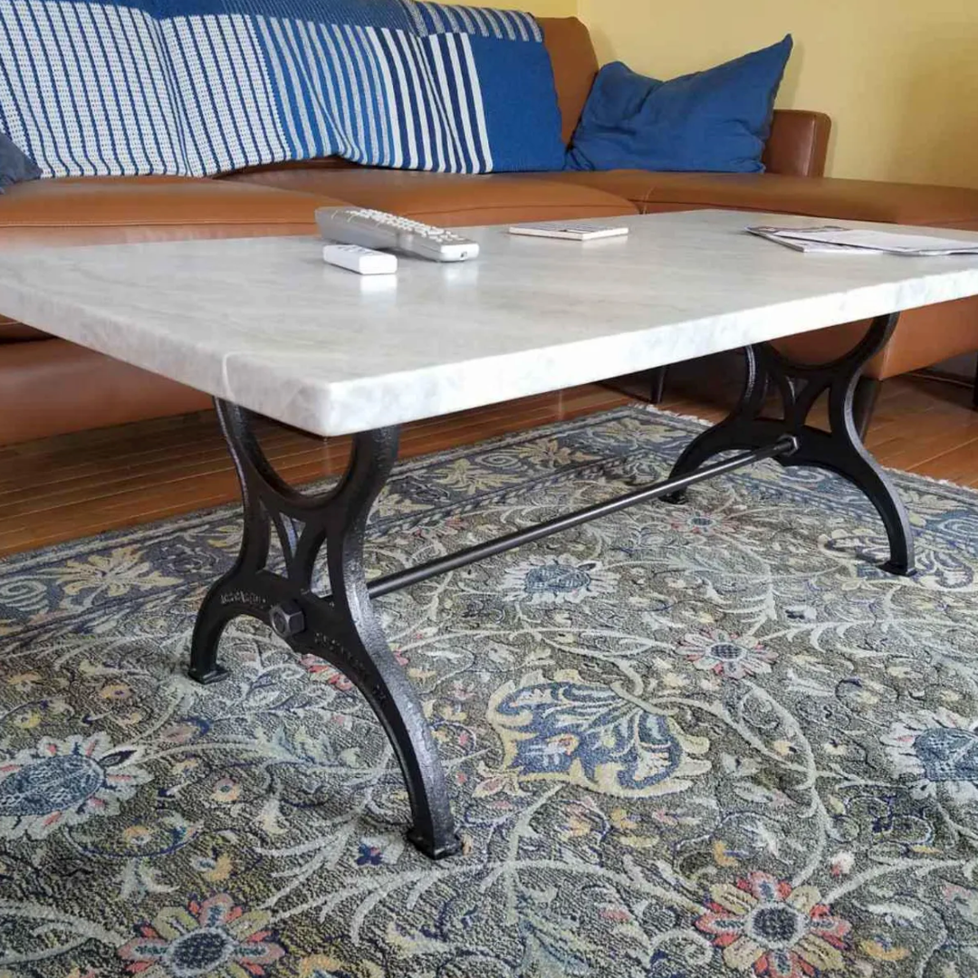 Black cast iron coffee table legs under a white stone top in front of a leather sofa