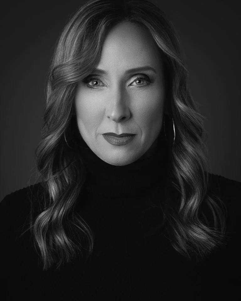 Black and white portrait of a woman with wavy hair, wearing earrings and a turtleneck, looking directly at the camera.