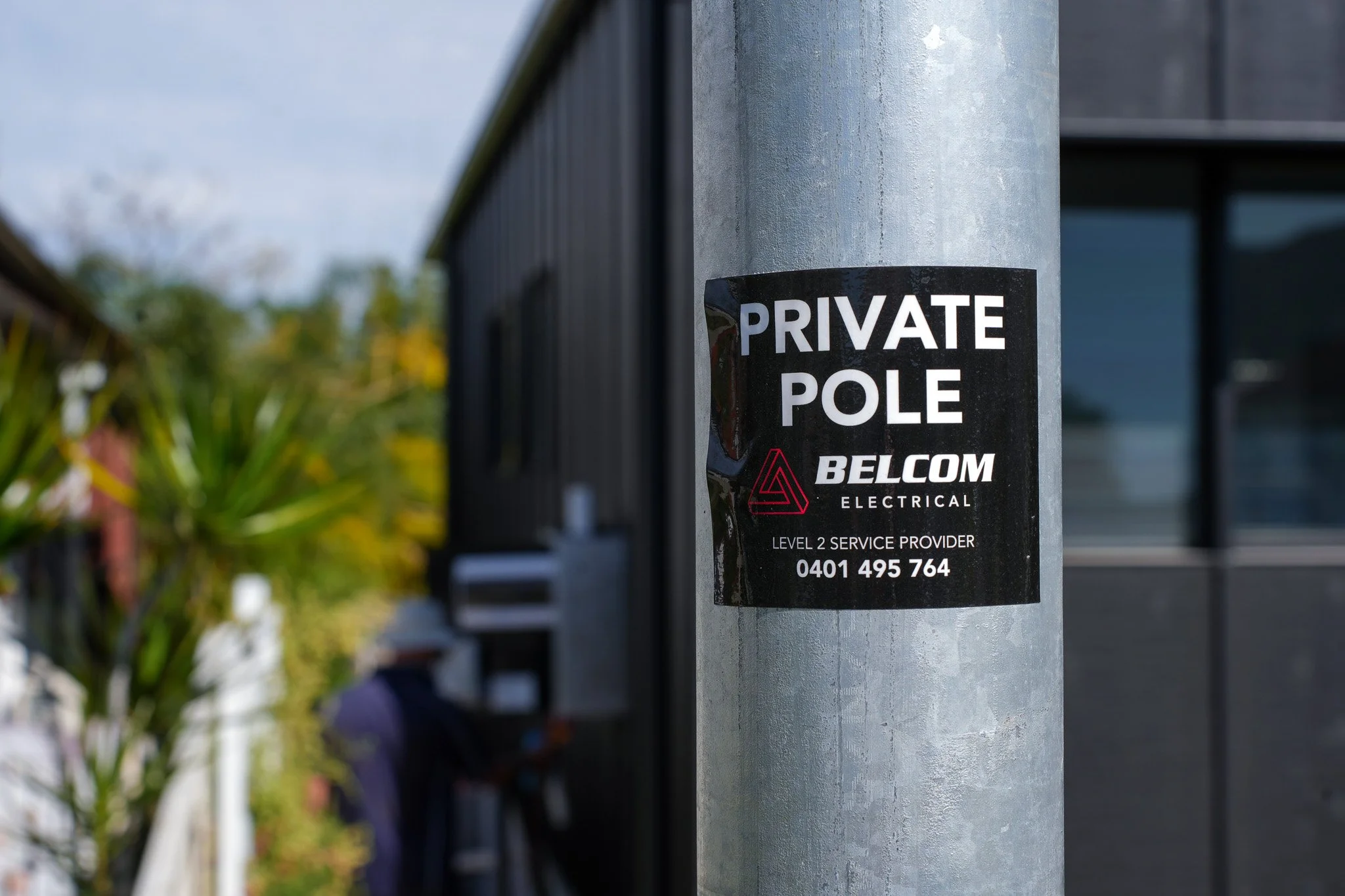 Sign on a gray pole that reads 'Private Pole' with the logo and contact information for Belcom Electrical, a Level 2 service provider, including a phone number.