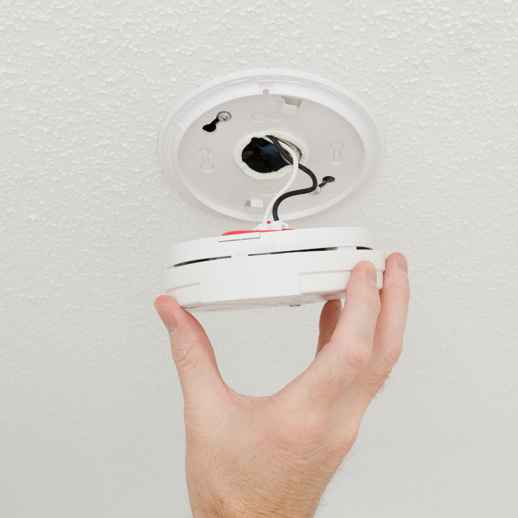 A person installing or maintaining a smoke detector on a ceiling.