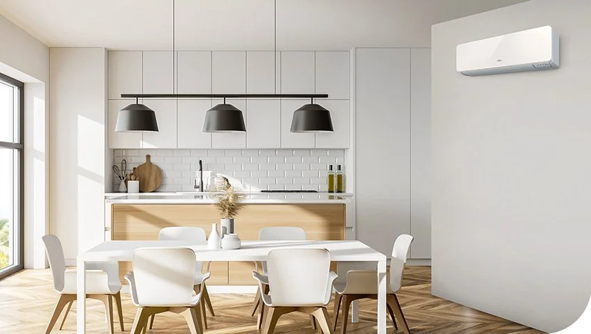 Modern dining room with white table and chairs, minimalist kitchen with white cabinetry, black pendant lights, and an air conditioner on the wall.