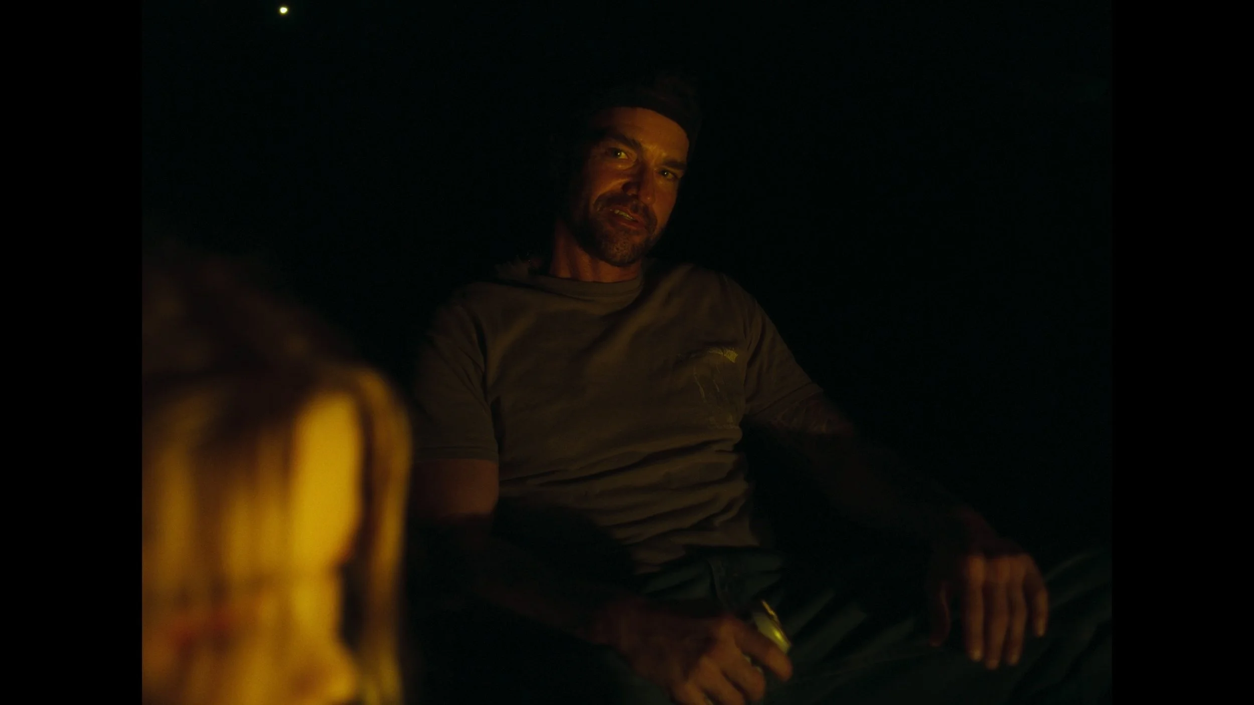 cinematic still frame from indie film, Openers, man sits at a fire pit, glowing from the warm light of the fire