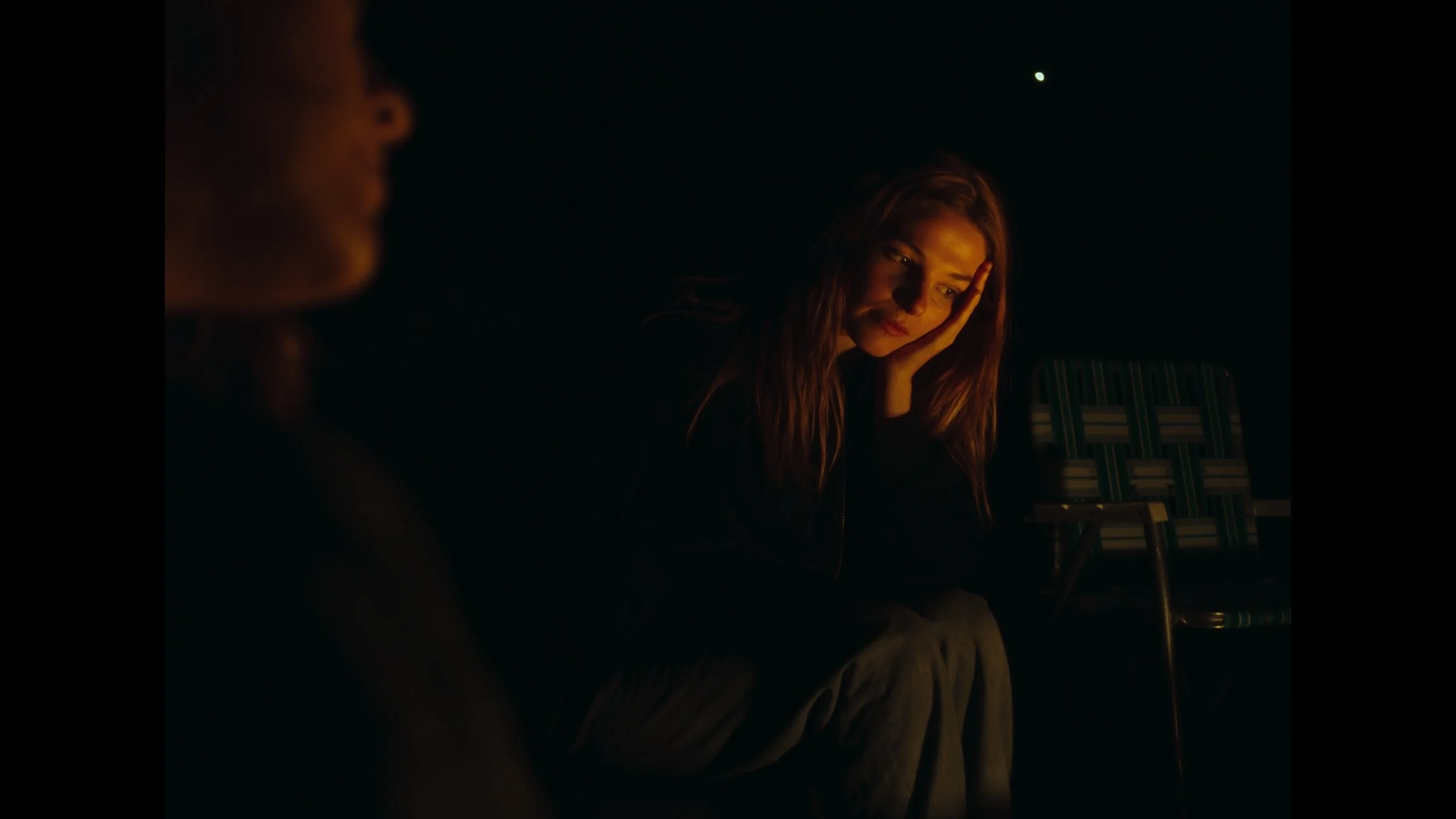 cinematic still frame from indie film, Openers, woman sits at a fire pit, her head in one hand, looking upset, glowing from the warm light of the fire
