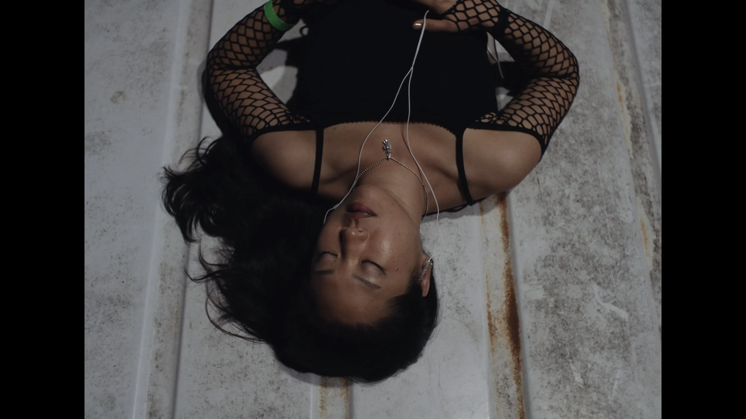cinematic still frame from indie film, Openers, overhead view of a woman as she lays on the roof of a van, eyes closed, listening to music in her earbuds