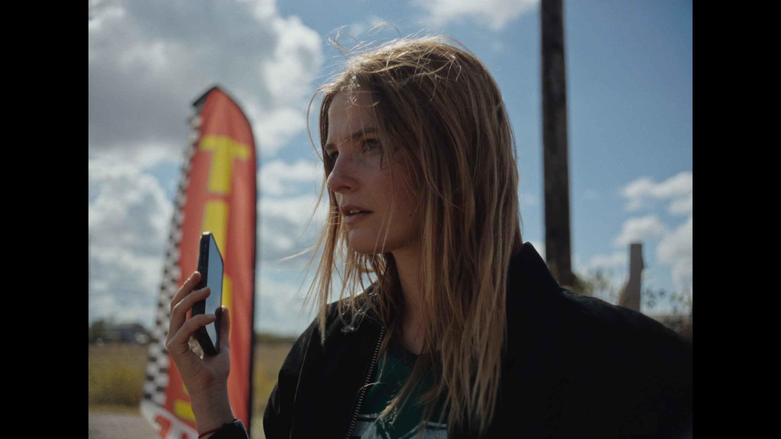cinematic still frame from indie film, Openers, woman stands outside in bright sunlight, holds phone away from her ear, she doesn't want to talk to the person on the other end of the phone call