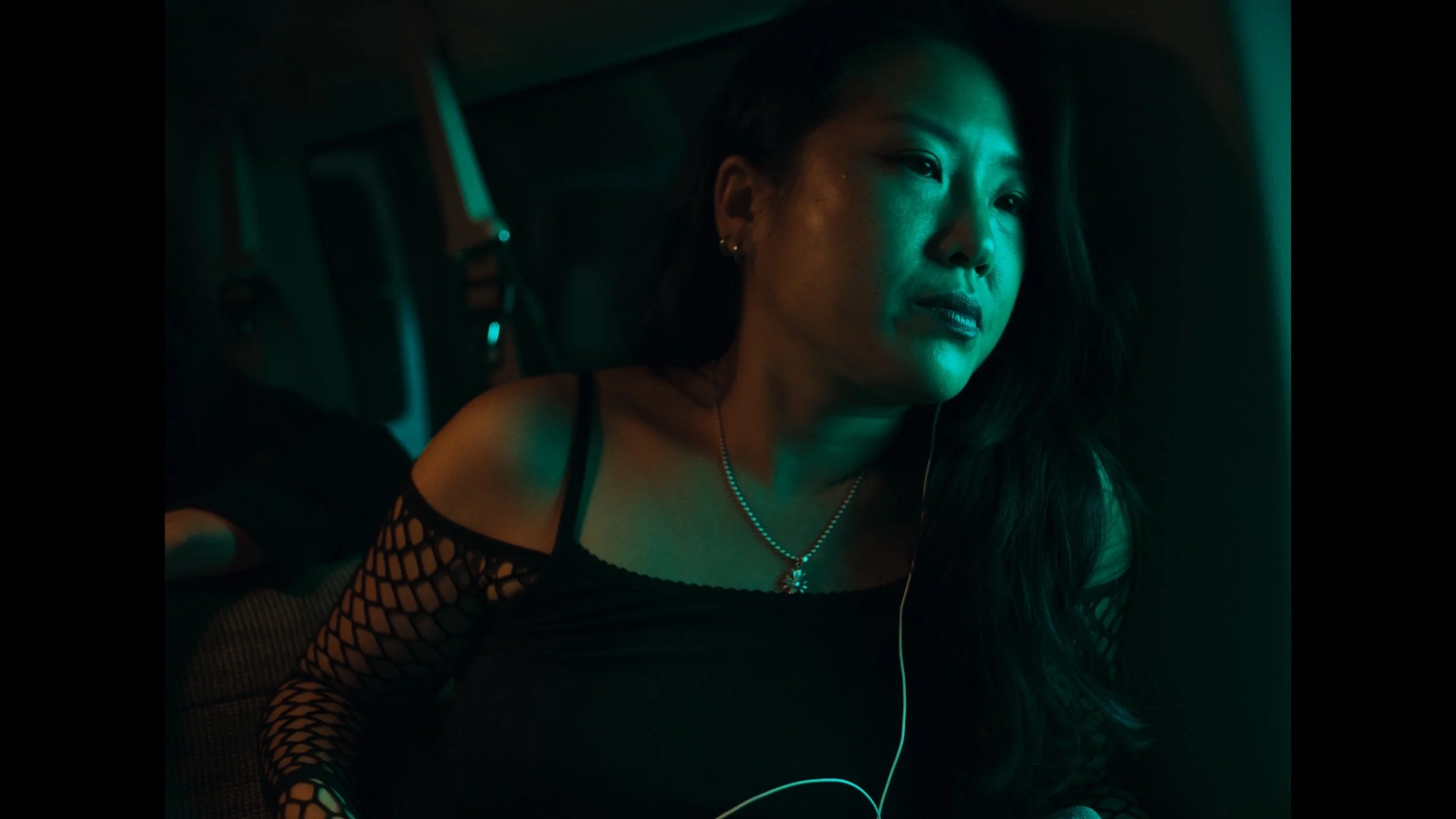 frame grab from the indie film Openers, woman washed in soft green light sits in van