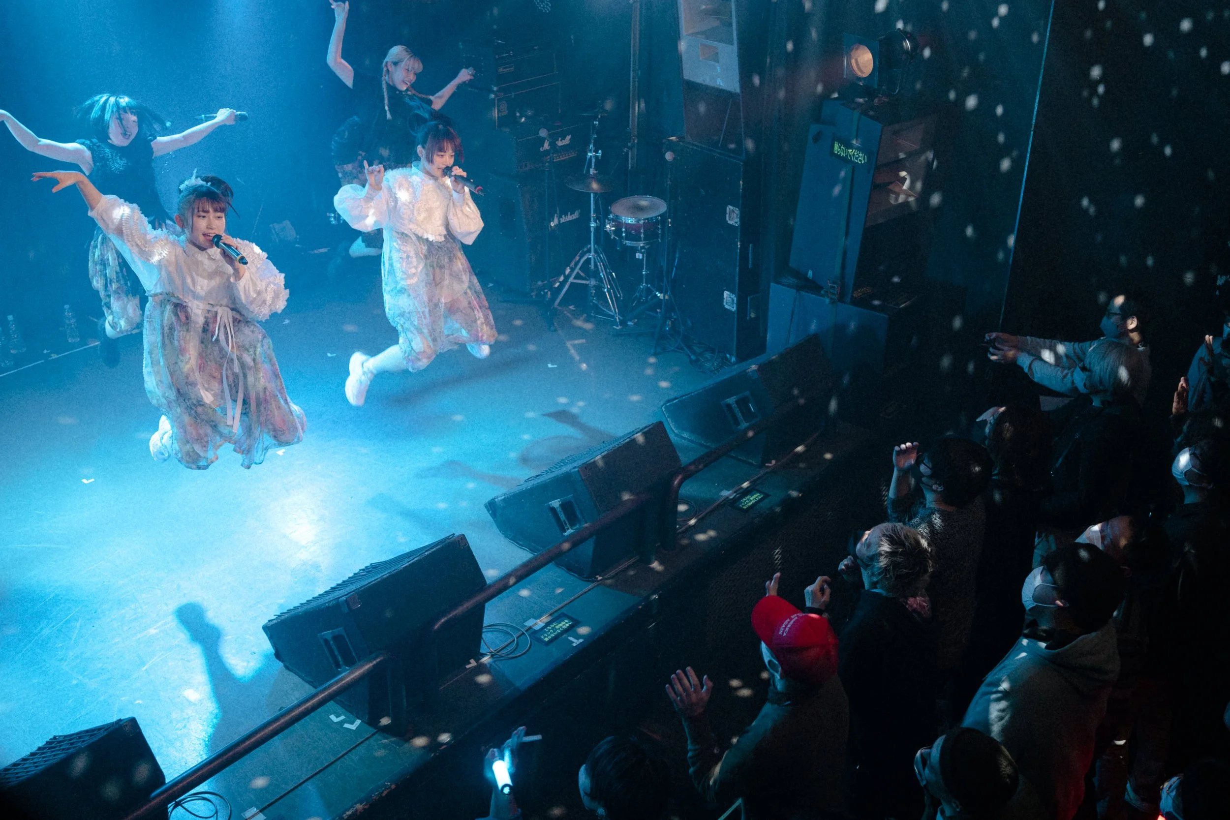 Overhead view of Japanese idol group performs on small club stage in Tokyo, Japan, four members all suspended in the air as the jump at the same time