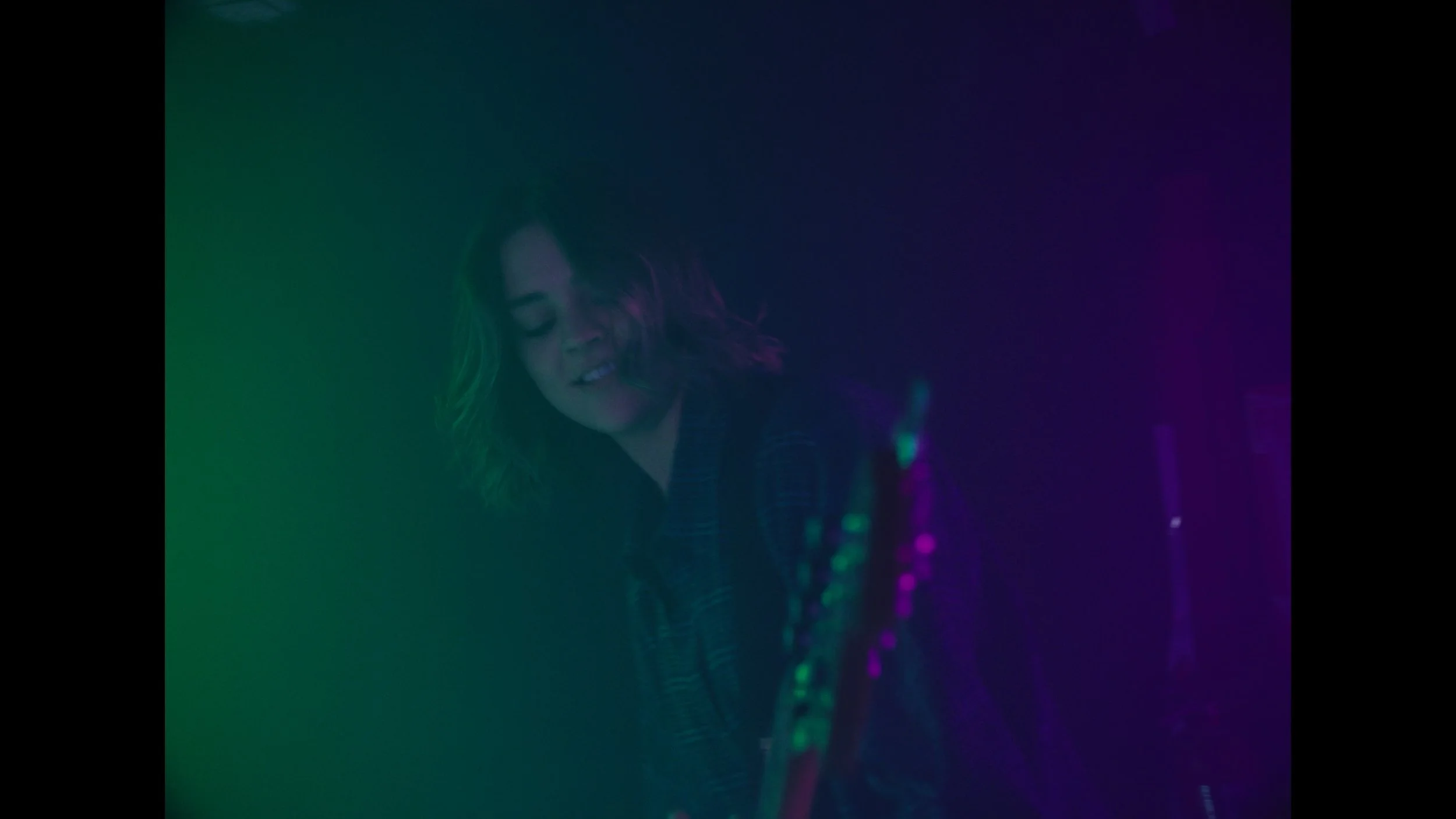cinematic still frame from indie film, Openers, woman washed in green and magenta stage lights, plays bass at rock show