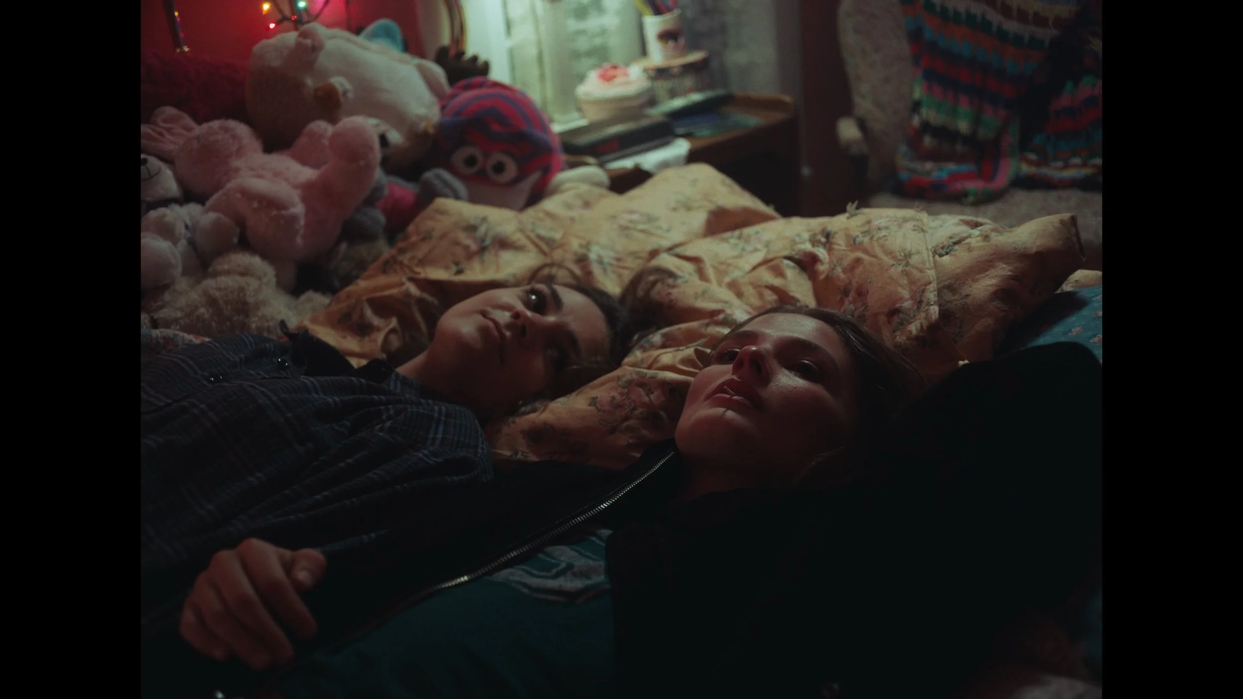cinematic still frame from indie film, Openers, overhead view of two women laying on a bed, surrounded by stuffed animals, they pensive