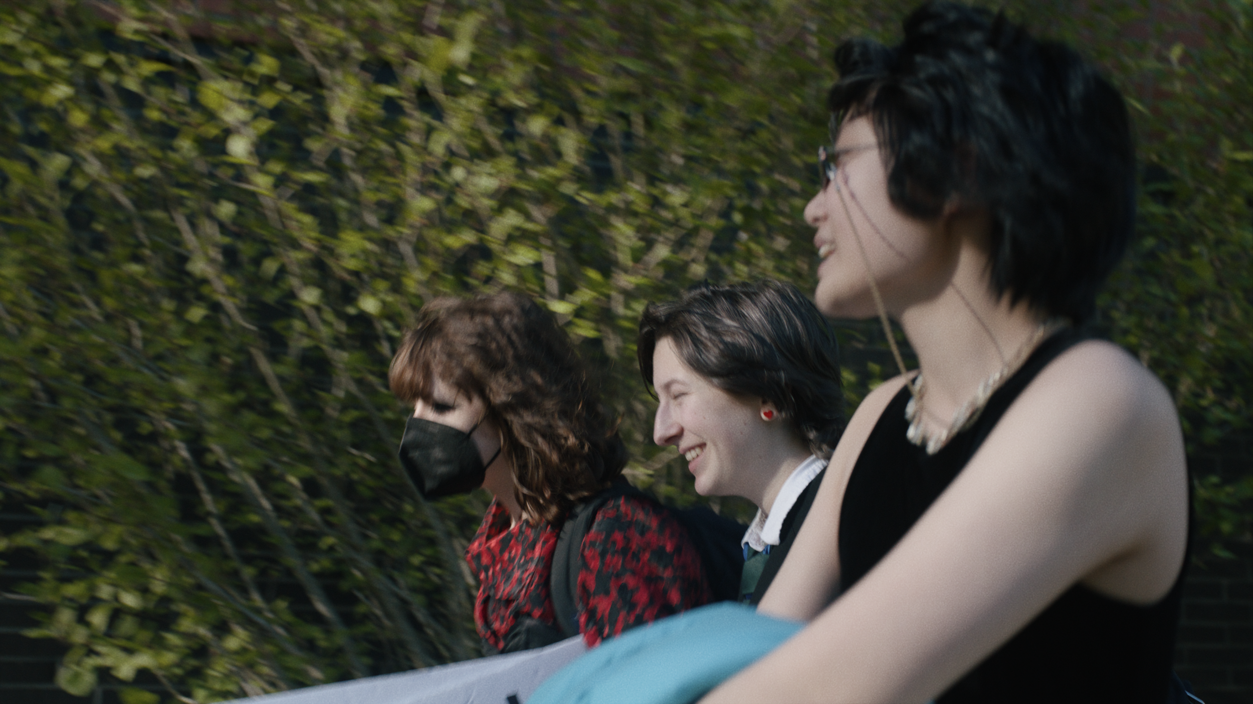 Documentary frame grab, three teenagers walk together outside, laughing and talking