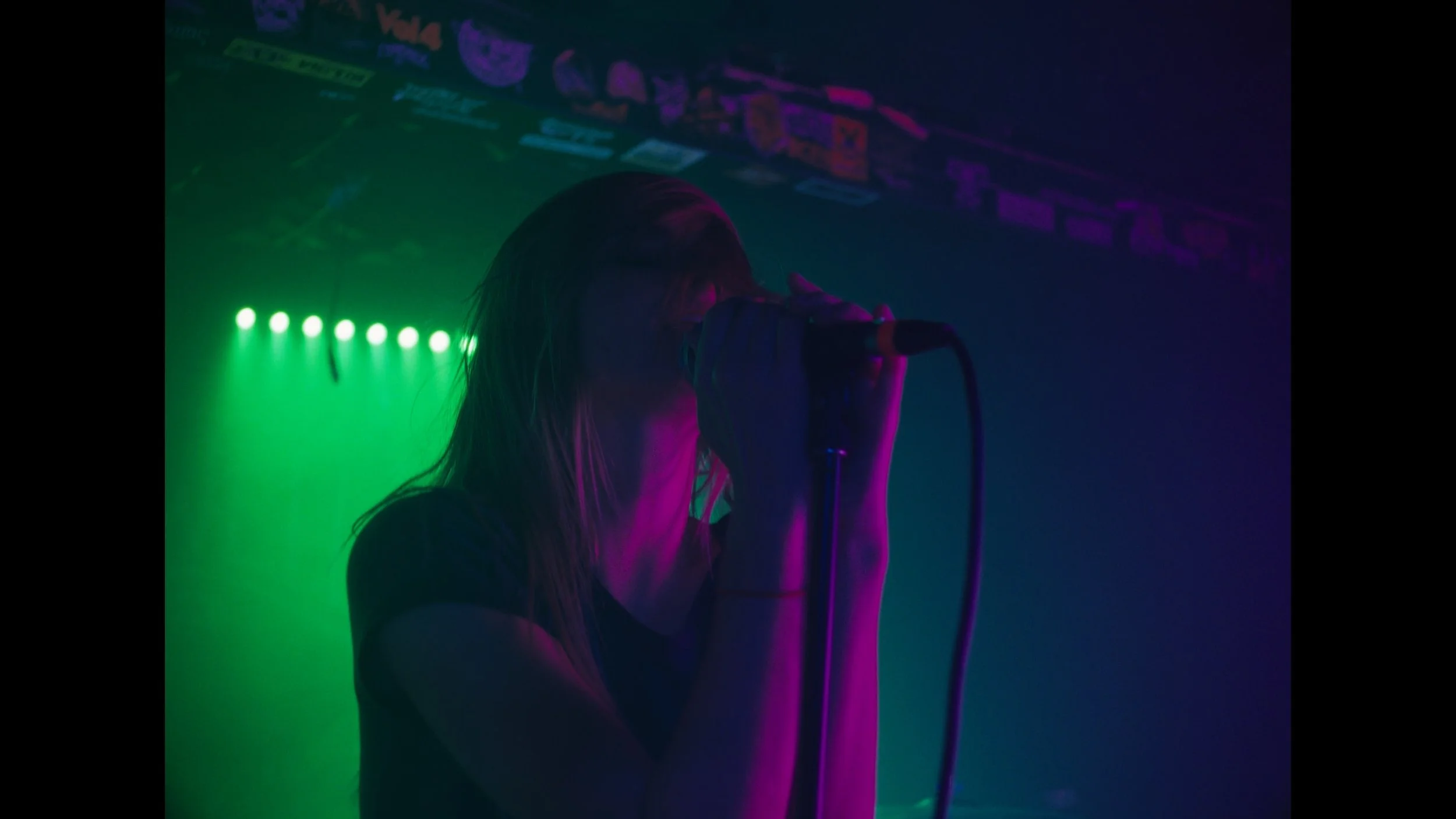 cinematic still frame from indie film, Openers, woman washed in green and magenta stage lights, sings passionately into microphone